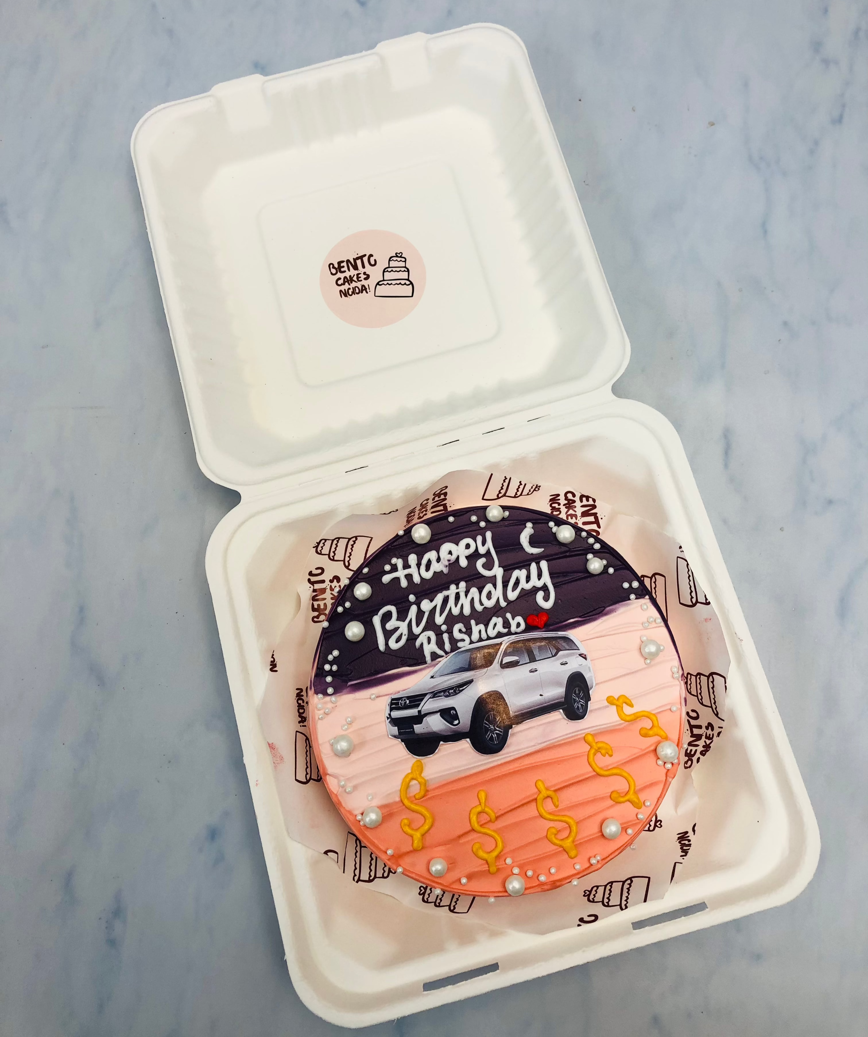 3 shades bento cake with a white Fortuner Car print and decorated withb dollar symbols.