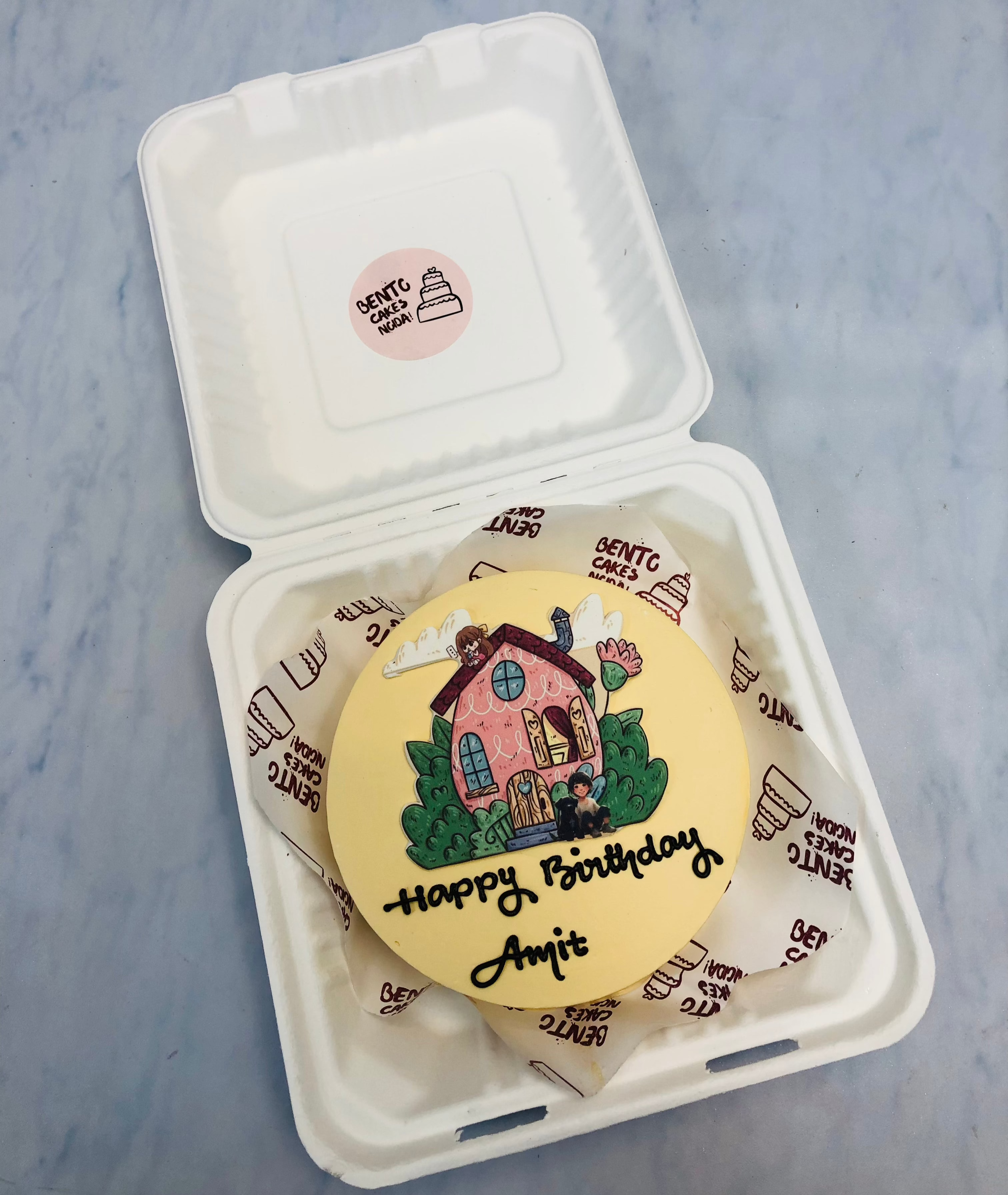 A light yellow bento cake having friend's home cartoon image on his birthday.