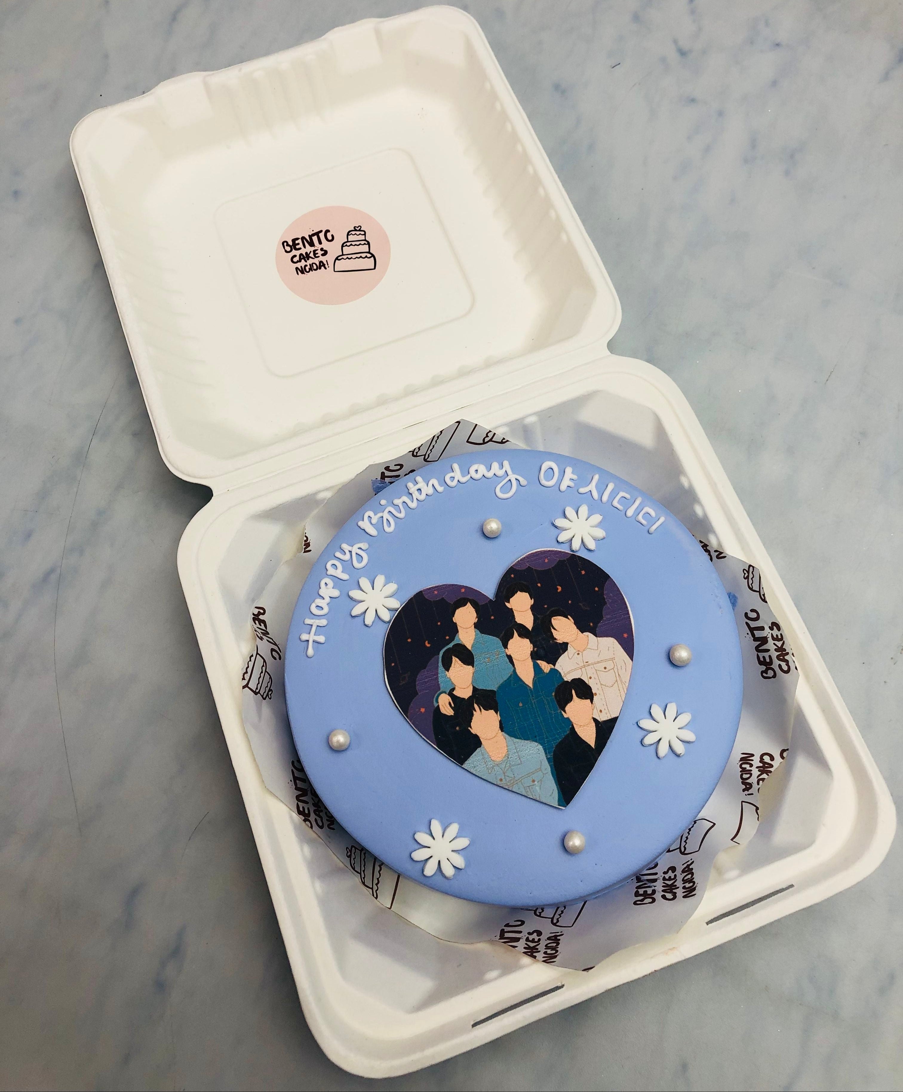 A friends theme blue bento cake having a sticker and white floral design.