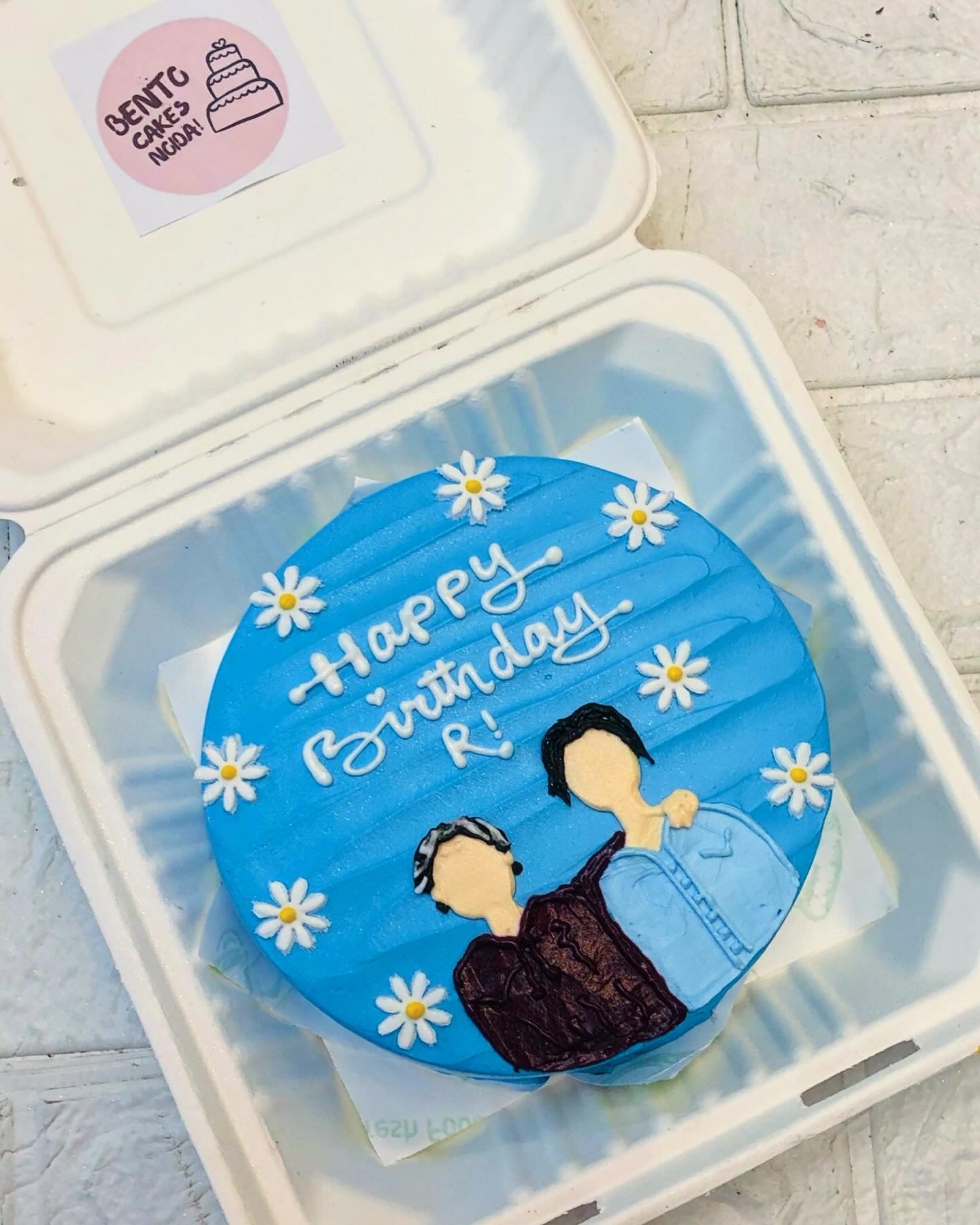 A blue bento cake having floral design with a men and womens friendship and celebrating birthday.