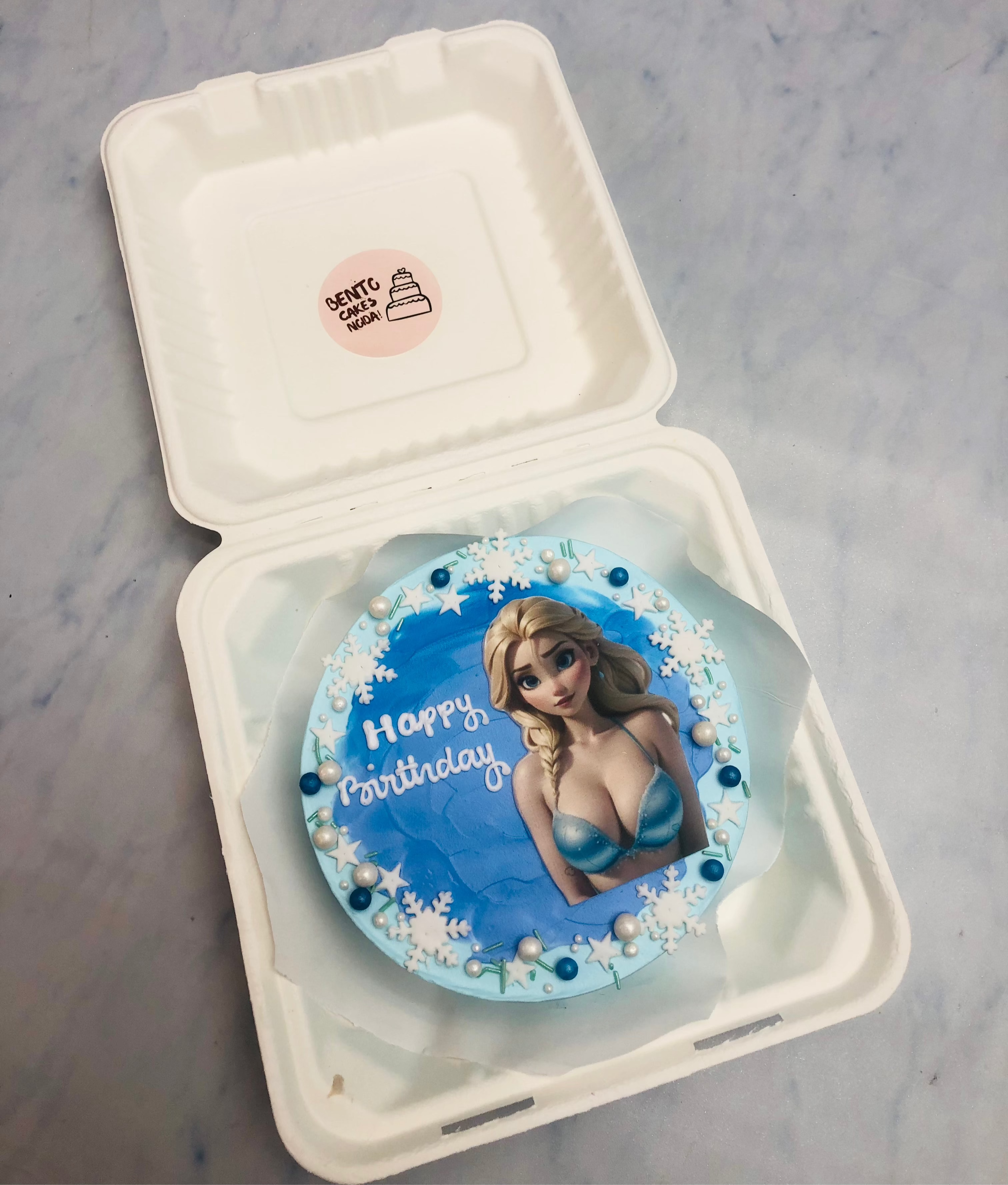 A beautifully crafted birthday cake with a blue theme, decorated with intricate snowflakes and pearls, presented inside a bento box.