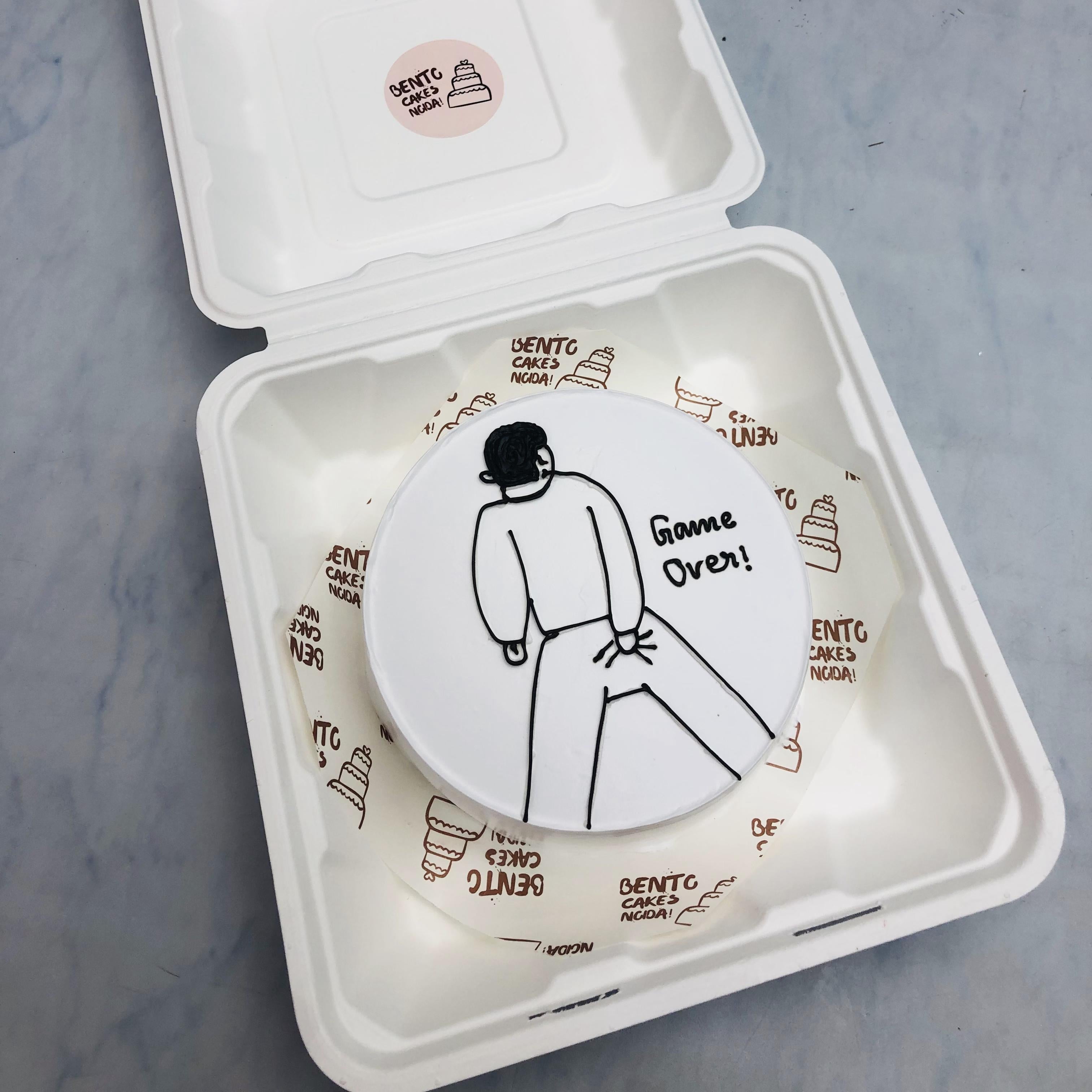 A white bento cake with a men sketch holding back with a text "Game Over!" on it.