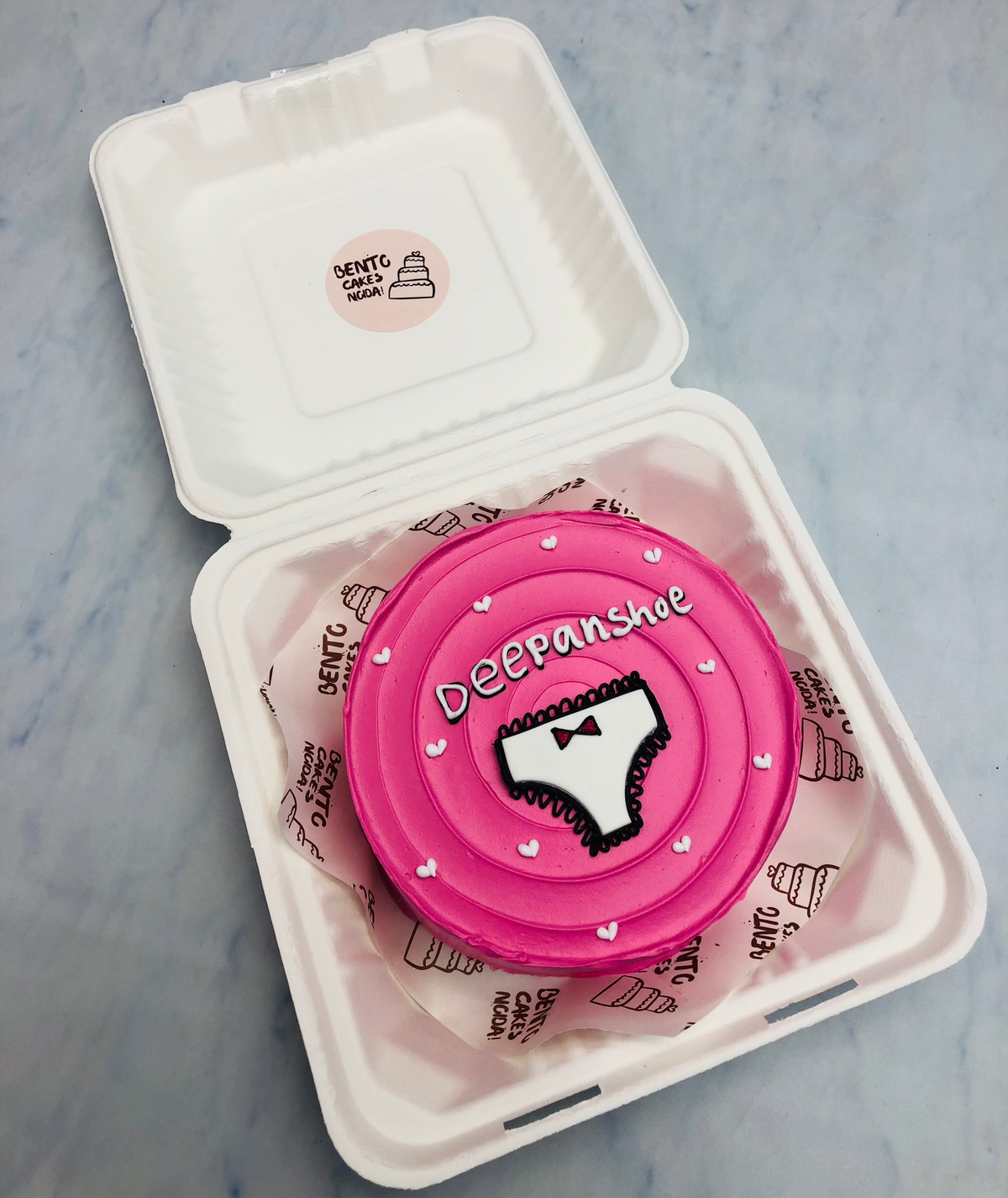 A pink bento cake with wavy design on top with a girls undergarments design.