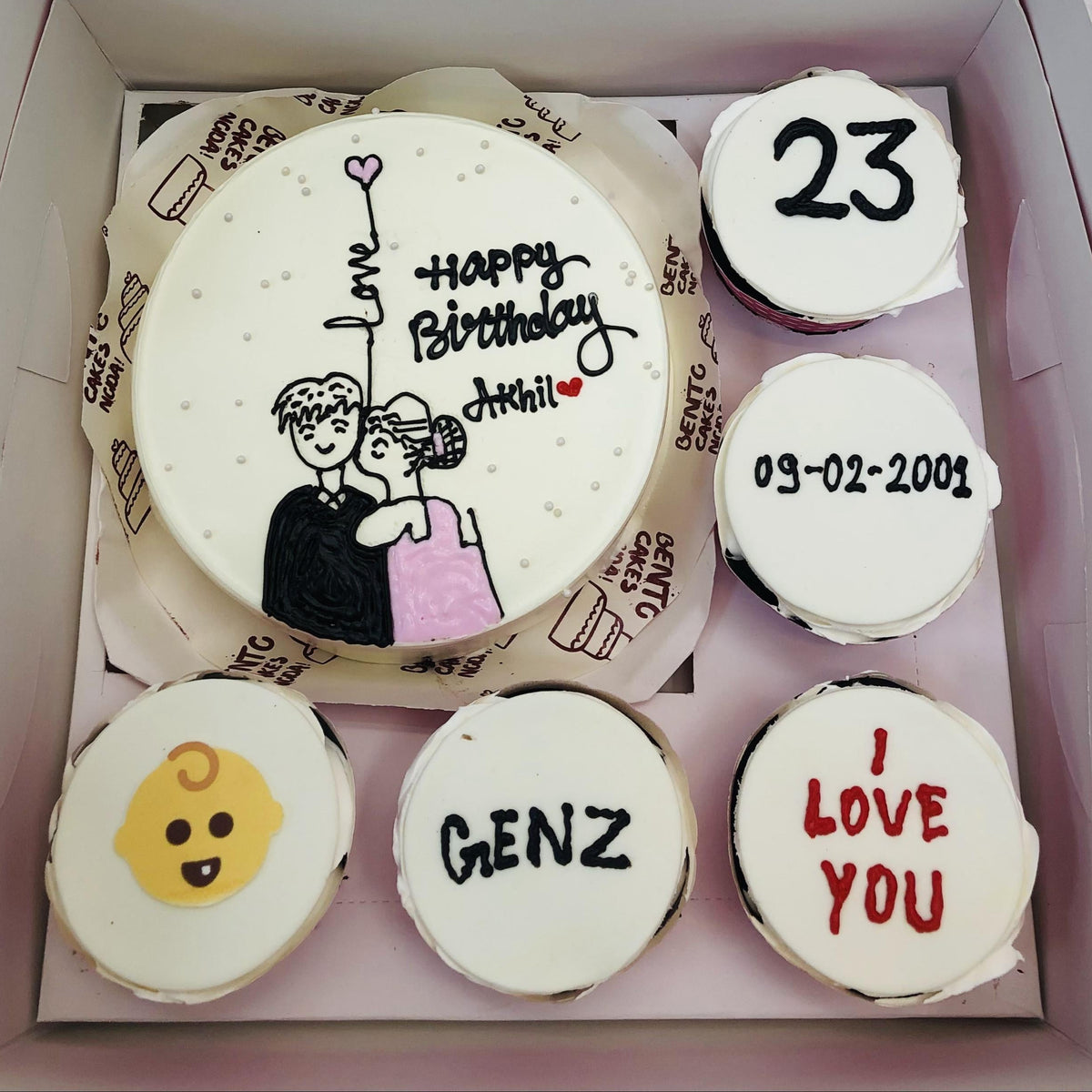 "A Gen Z-themed bento combo cake set featuring a large round cake with a drawing of a couple holding a balloon and five small cupcakes with unique decorations, including 'GENZ,' '23,' a baby face emoji, a date '09-02-2001,' and 'I LOVE YOU.'"
