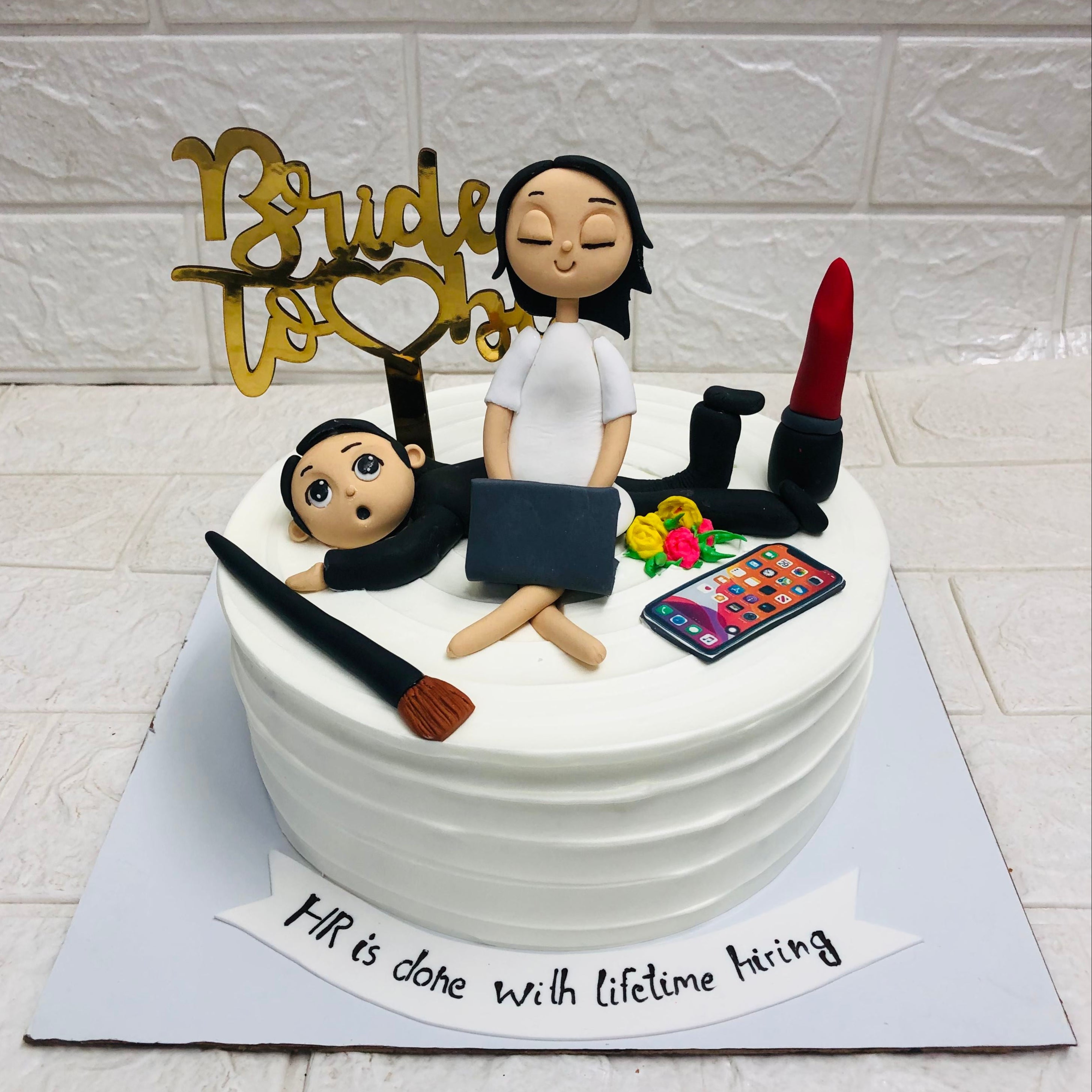A whimsical cake featuring a woman sitting atop it, another woman holding a laptop, and a sleepy man nearby.