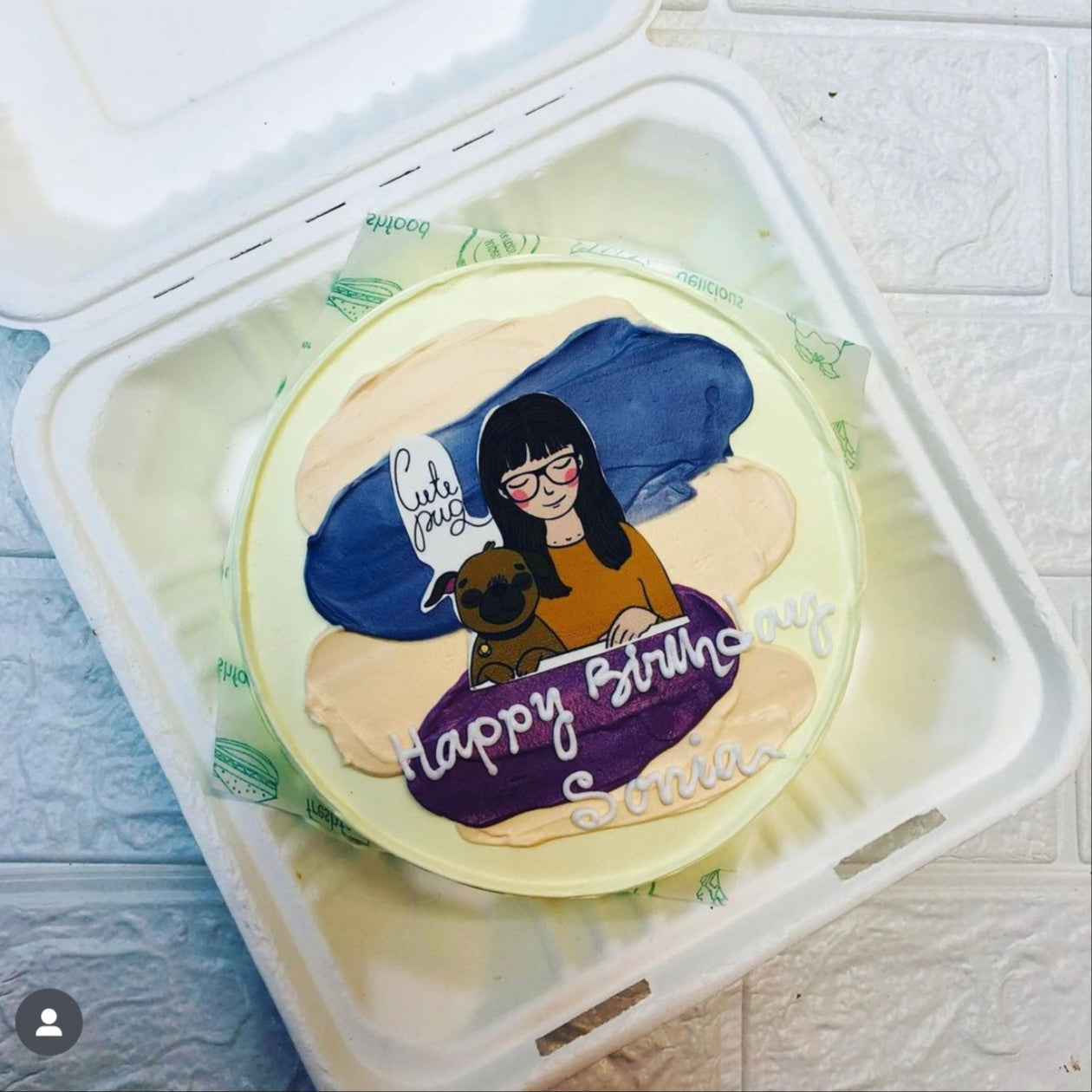 A round birthday cake with colorful icing and a custom illustration of a person holding a dog. The cake is placed inside a bento box. The text on the cake reads "Happy Birthday Sonia" and "Cute Dog."