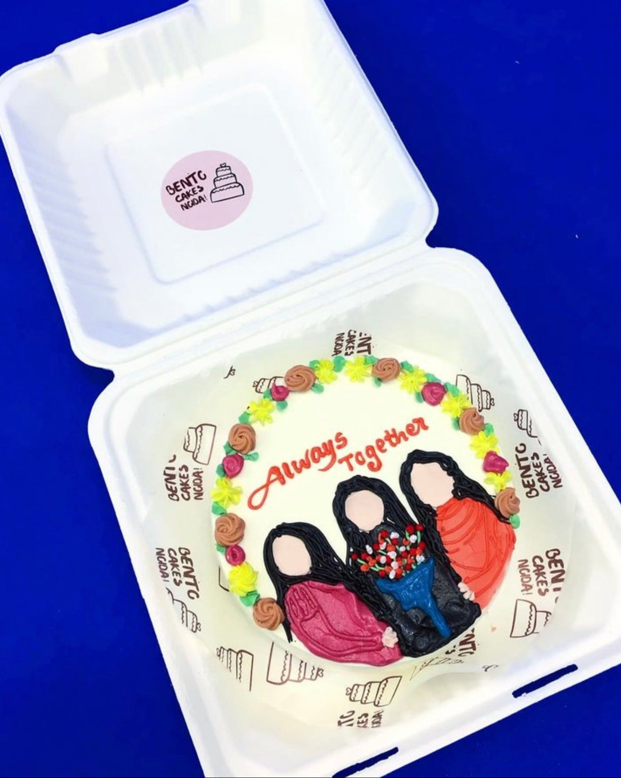 A white bento cake with 3 friends design with colorful florals on it's boundary and they are celebrating their bonding.
