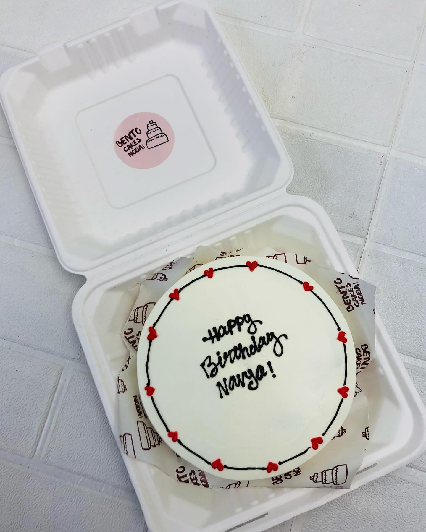 A white bento cake decorated with red hearts on boundary and a text written with black icing.