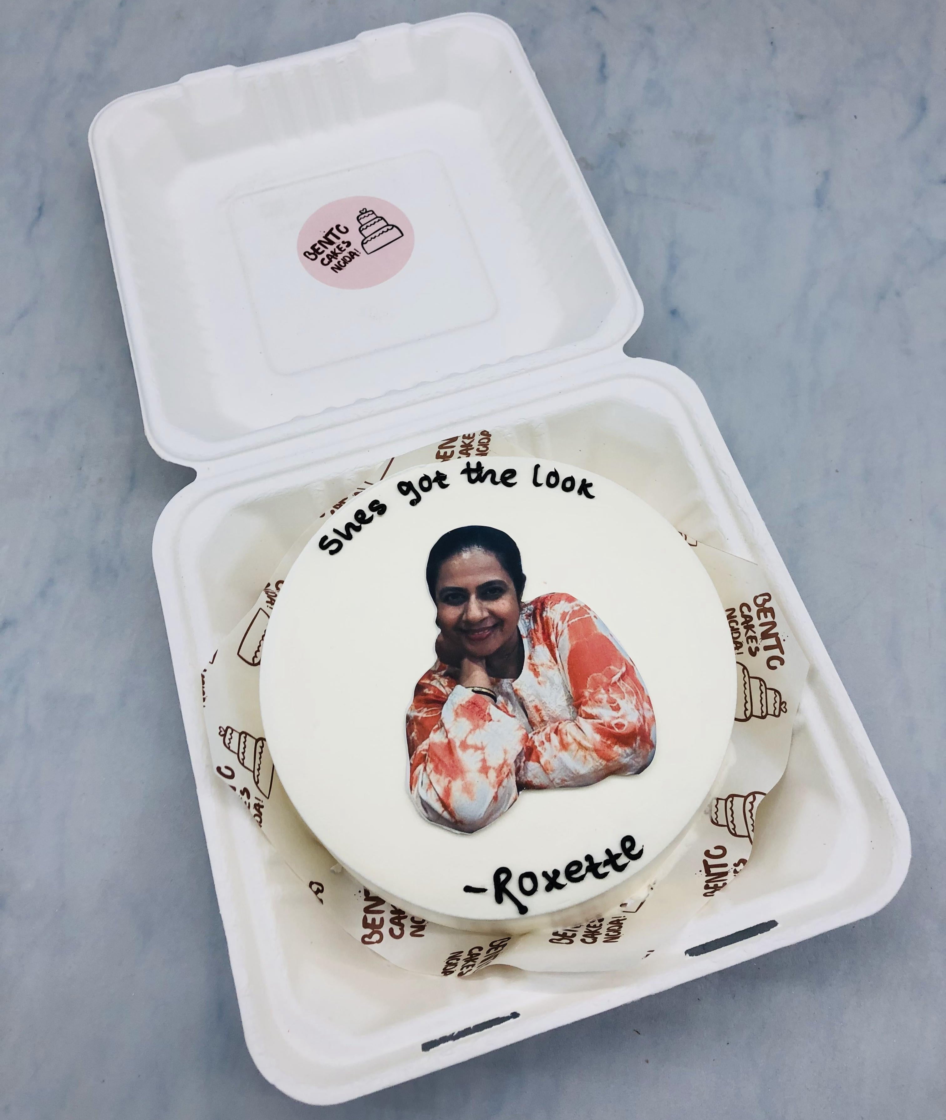 A white bento cake with a birthday girls photo and a text written with black icing.