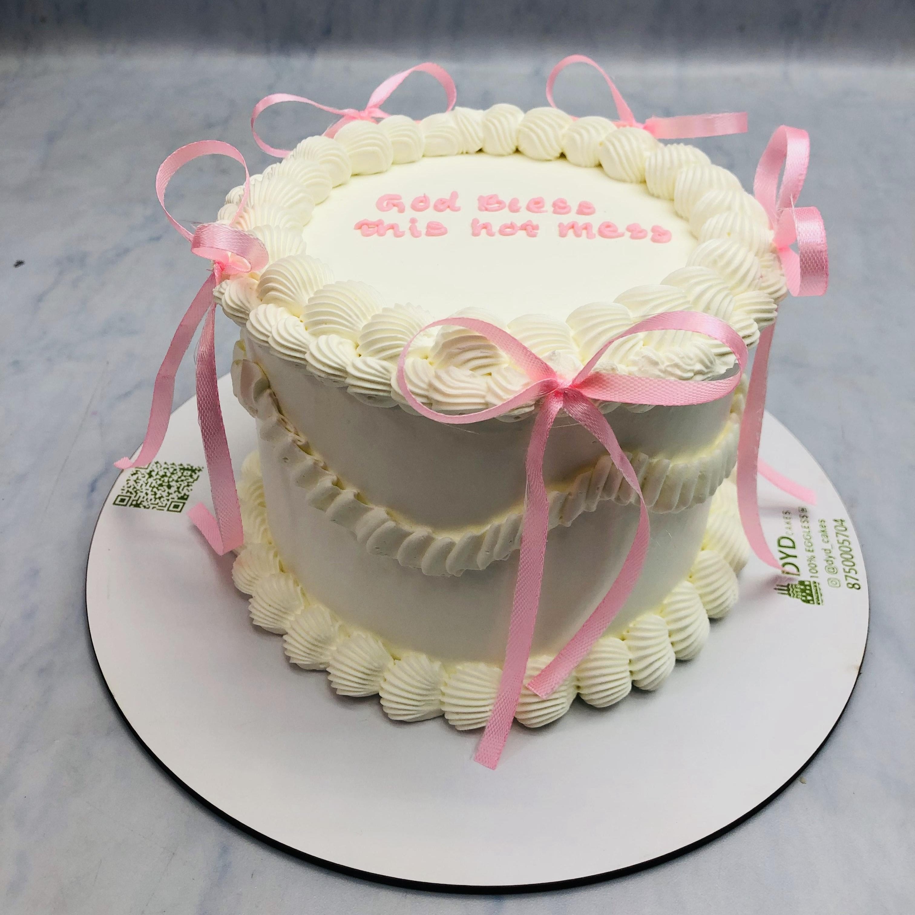 A birthday cake adorned with pink ribbons and a cheerful "God Bless This Hot Mess" message on top.