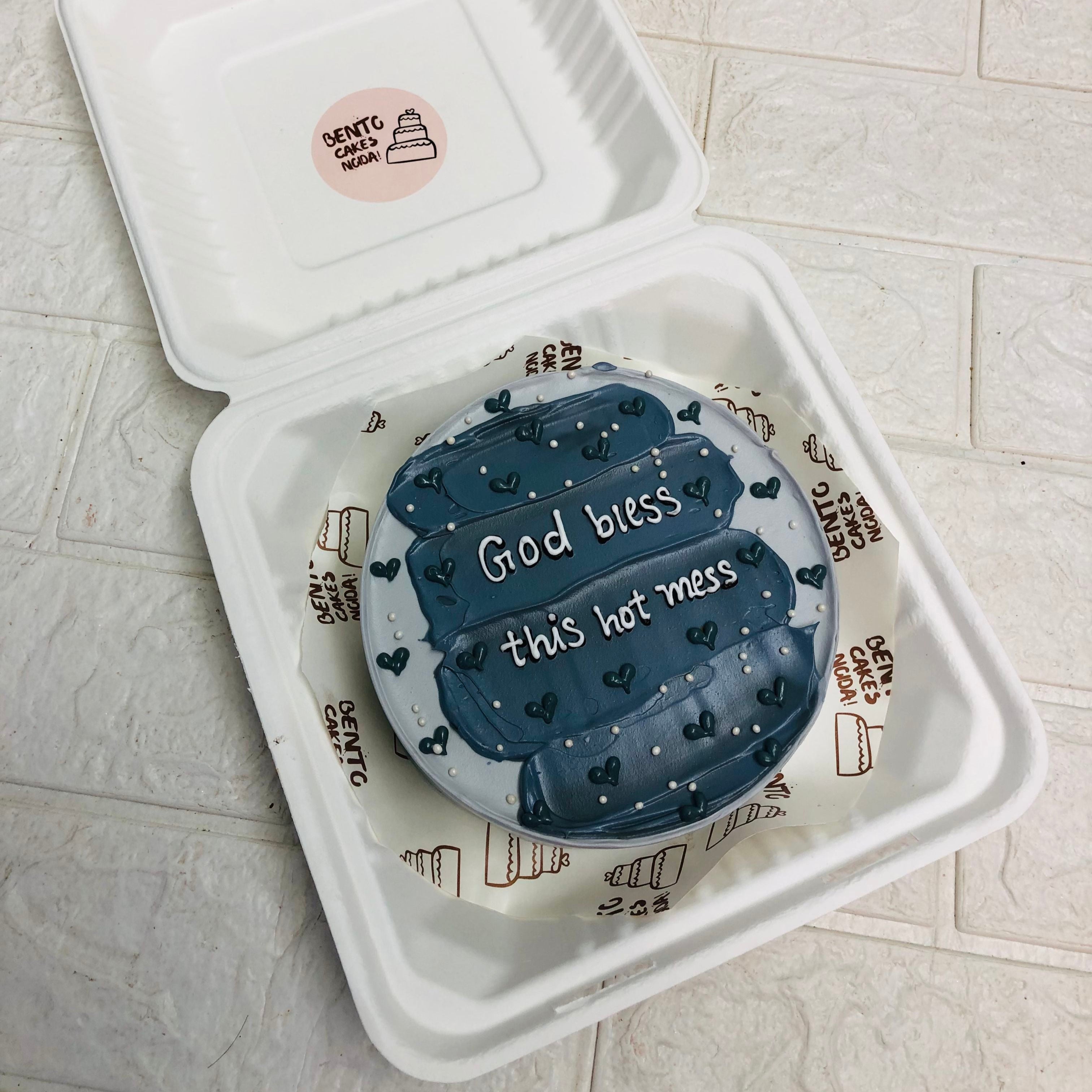 A box containing a grey cake and a note that reads "God bless this hot mess," symbolizing a thoughtful gesture of kindness and love.