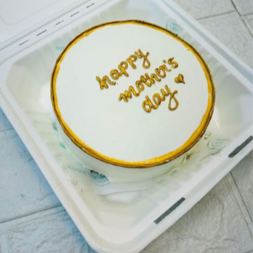 A white cake with golden boundary and a text "happy mother's day" with golden color on it.