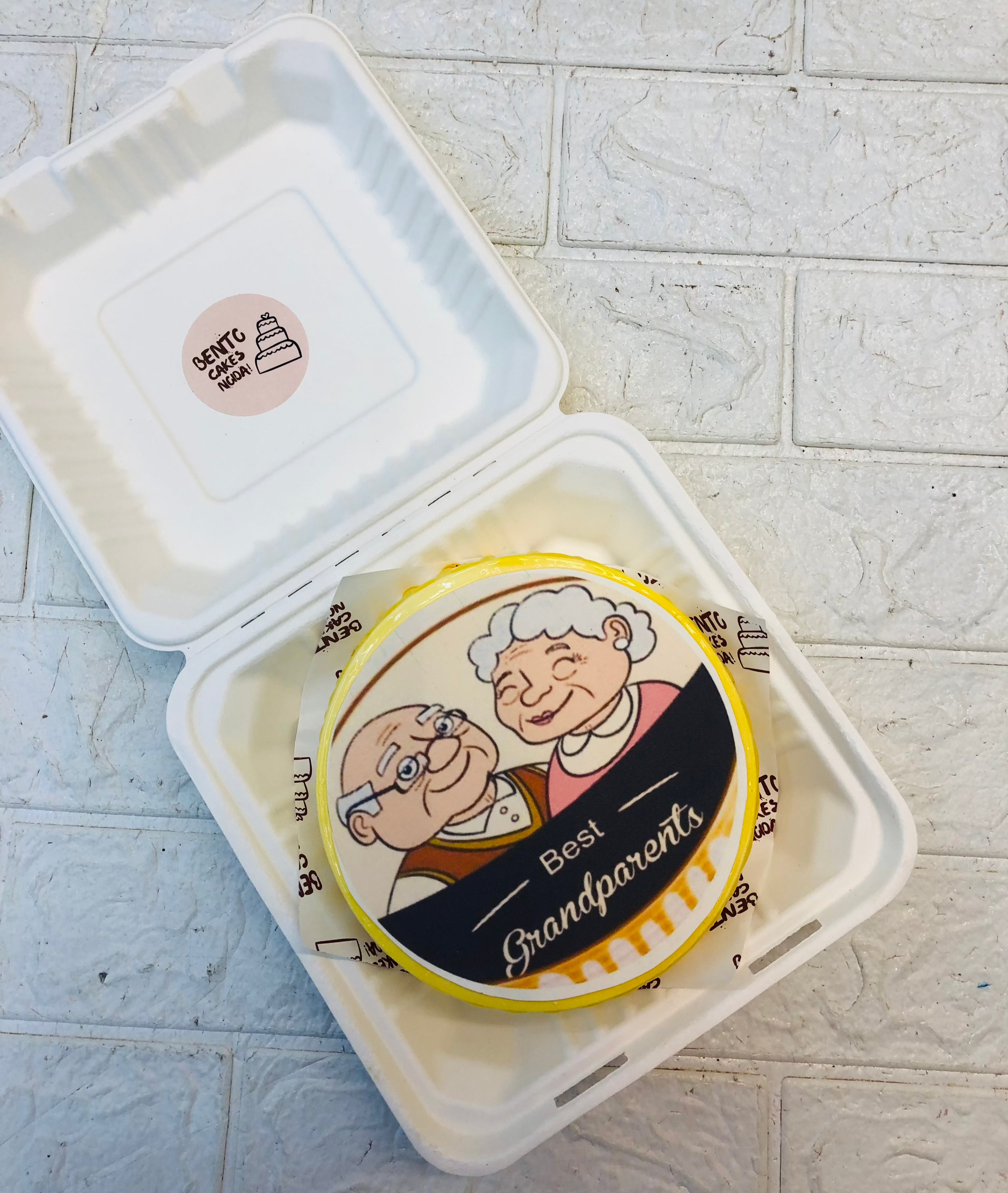 A yellow bento cake having best grand parents cartoon image on cake.
