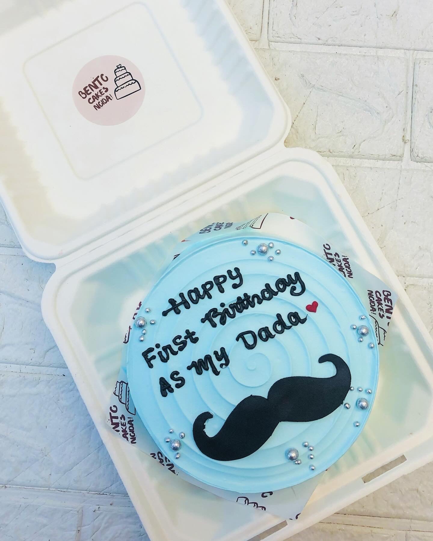 A cool blue bento cake having wavy design on top with a mens mustaque and a text written with black icing.