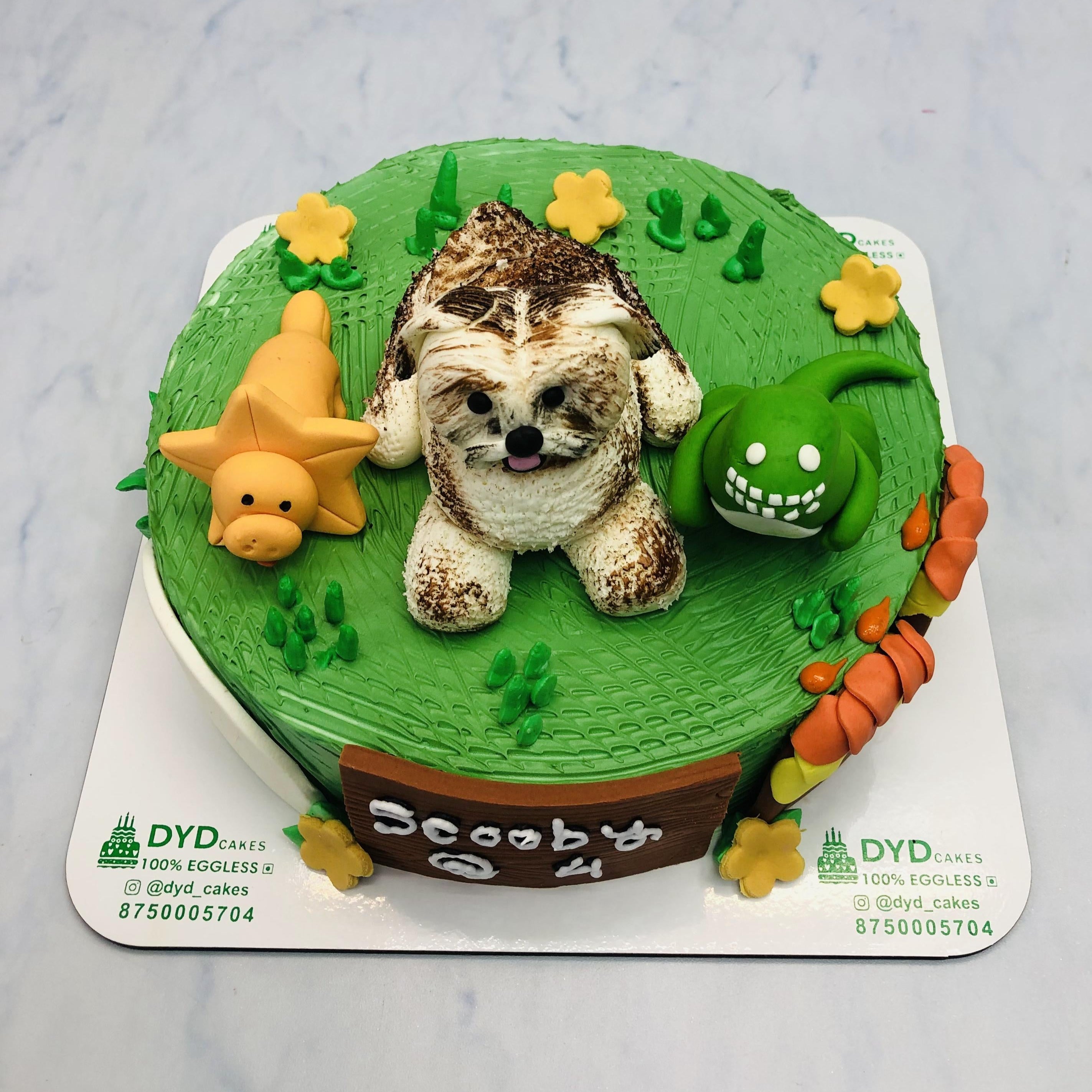 A green birthday cake with a dinosaur and star decoration, featuring the text 'Scooby @ 4' on a wooden sign.