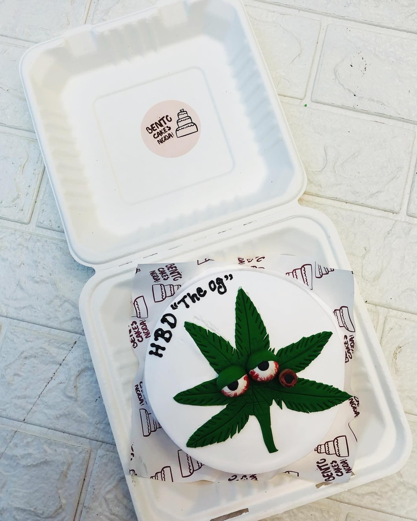 A green weed leaf design on a white bento cake with a text "HBD 'The og' written on it.