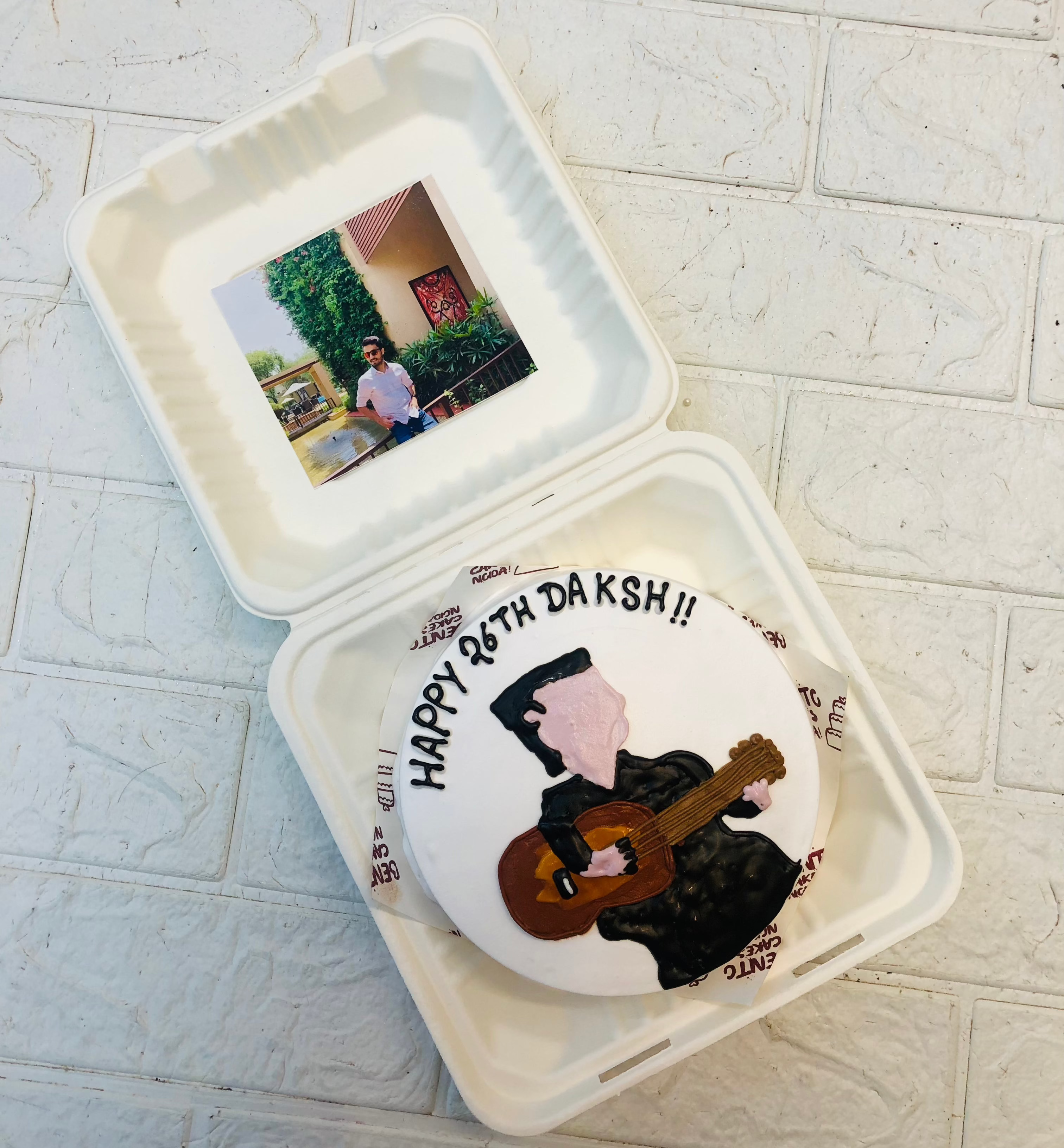A white bento cake having a man playing guitar design with a photo of birthday boy.