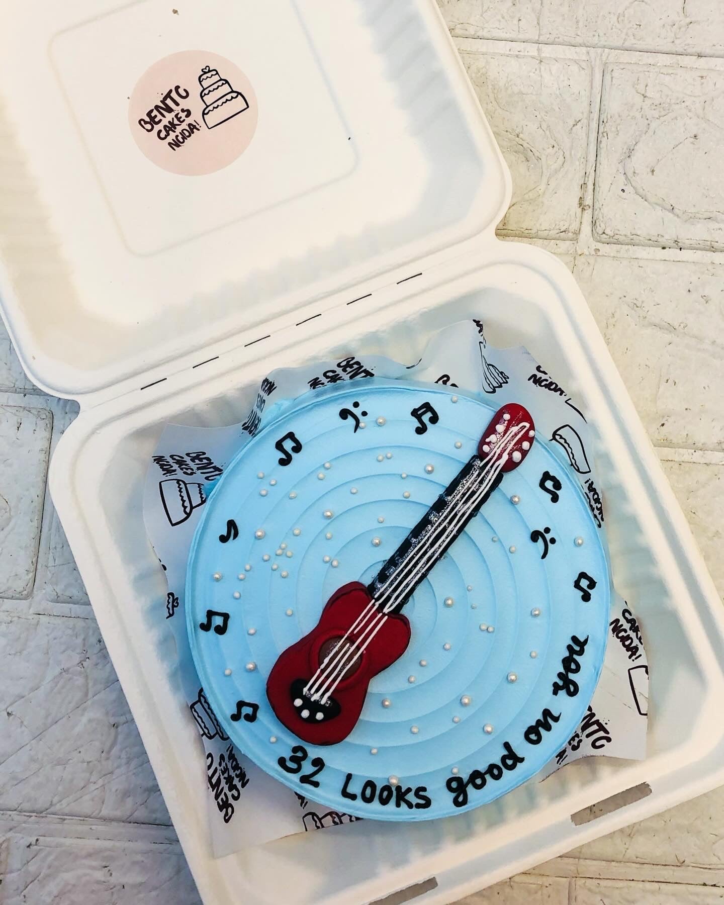 A cool blue bento cake is designed with a guitar and musical tune all arround the cake for guitar lover's birthday.