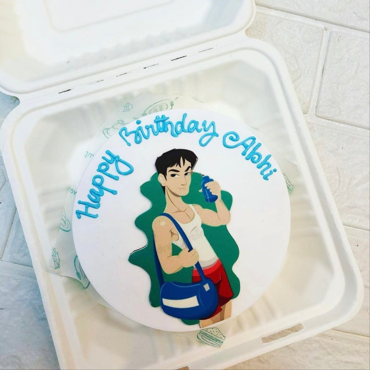 A round birthday cake with a custom design featuring a person holding a drink and a bag, with the text "Happy Birthday Abhi" written in blue icing.