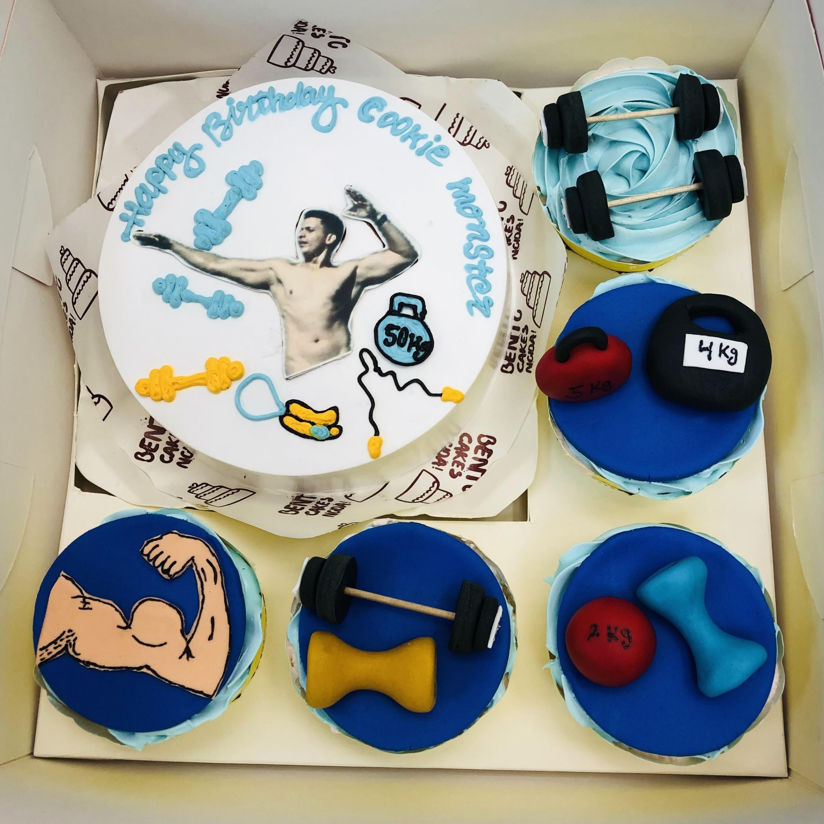A gym-themed bento combo cake set with a central round cake featuring gym items like dumbbells, a kettlebell, barbell, jump rope, and a photo, surrounded by five cupcakes decorated with fitness-themed fondant toppers.