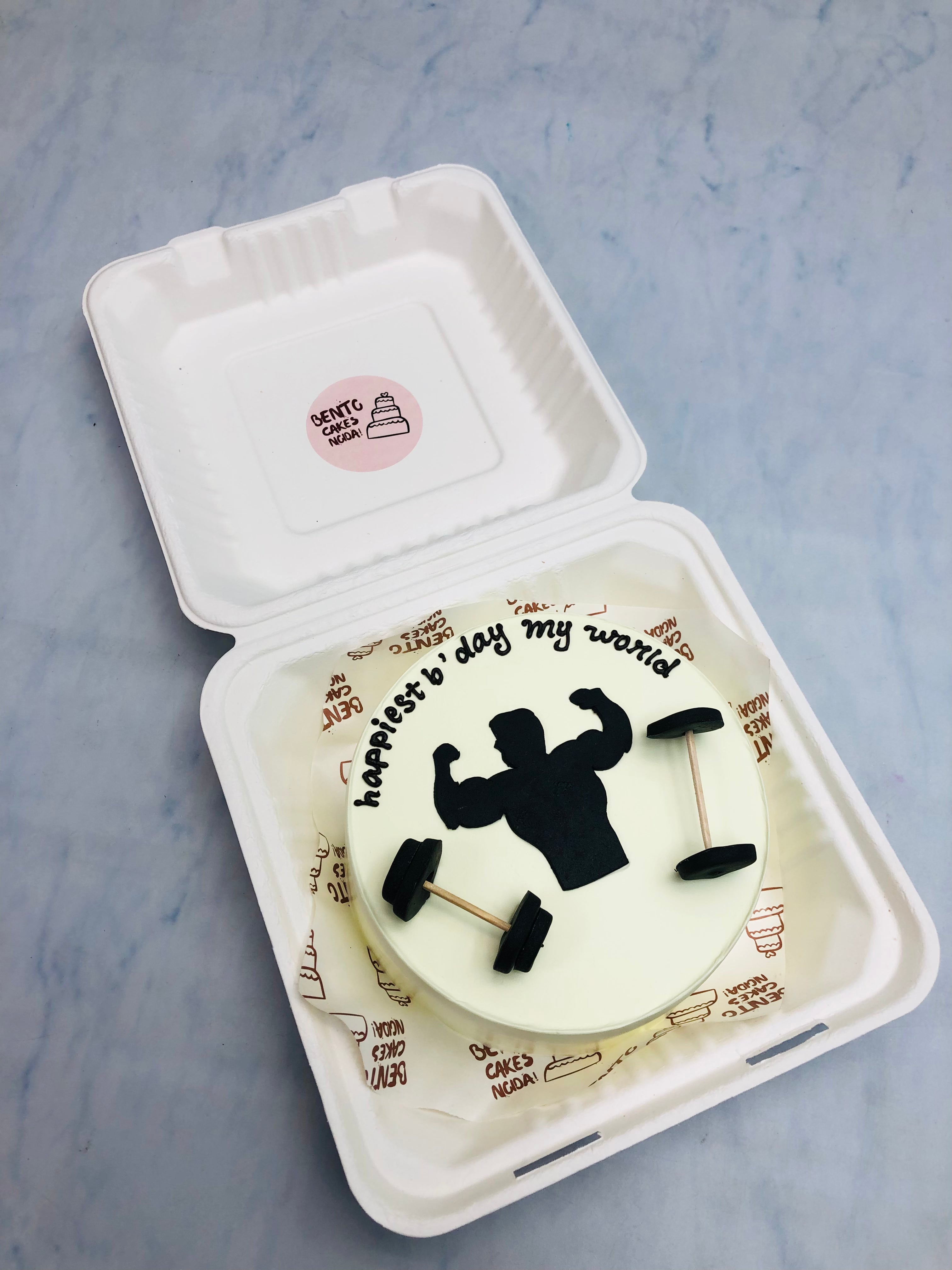 A white bento cake with a gym lover fondant man with his dumbles.