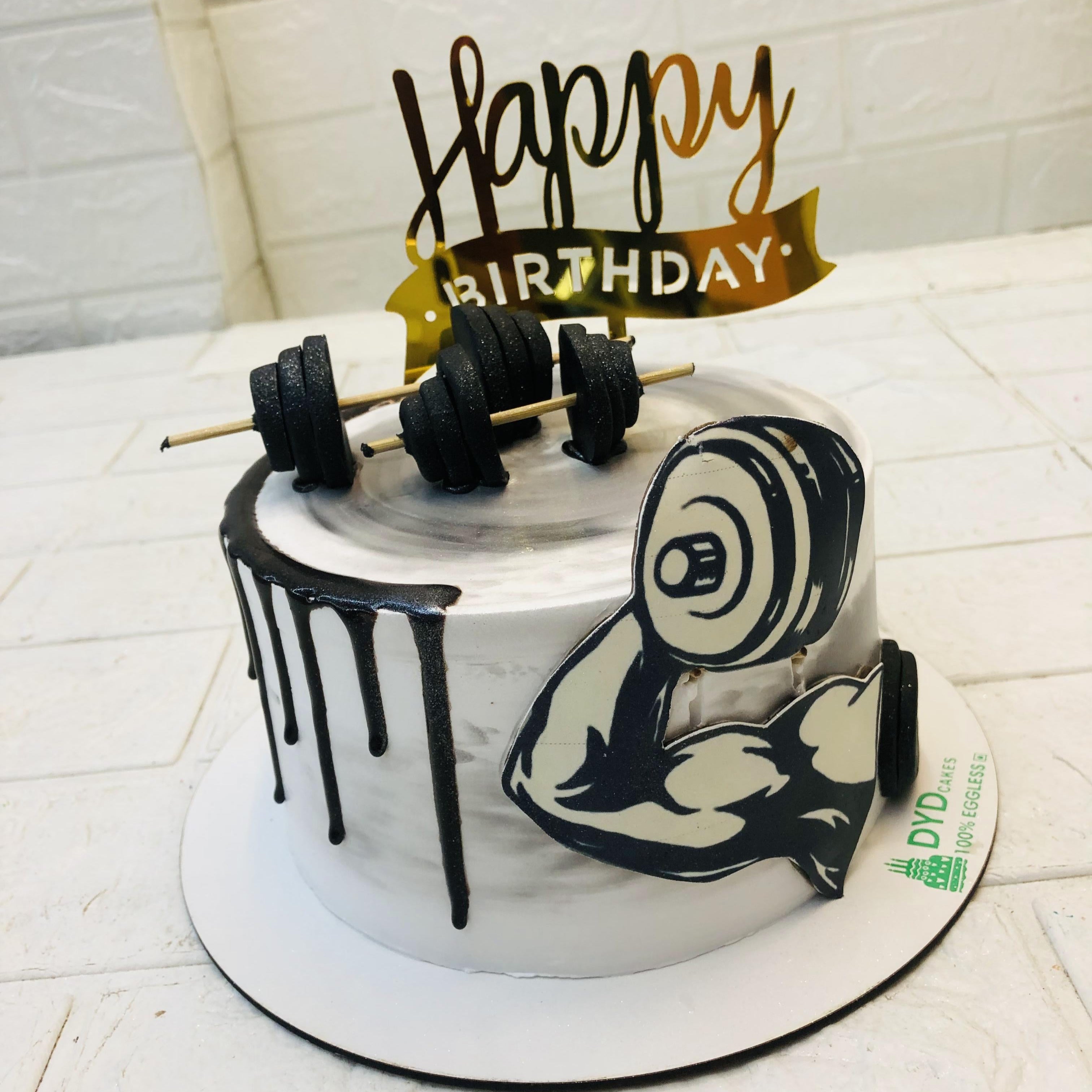 A birthday cake featuring a white and black design, with gym dumbbells design on top for a fitness-themed celebration.