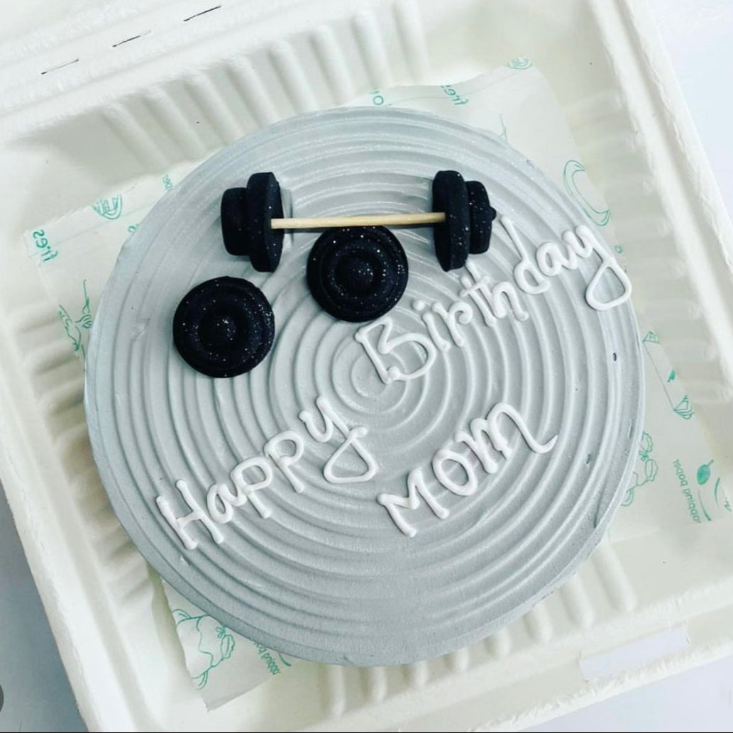 A delightful birthday cake inside a bento box, featuring a bright "Happy Birthday Mom" sign on top with Gym Dumble shapes.
