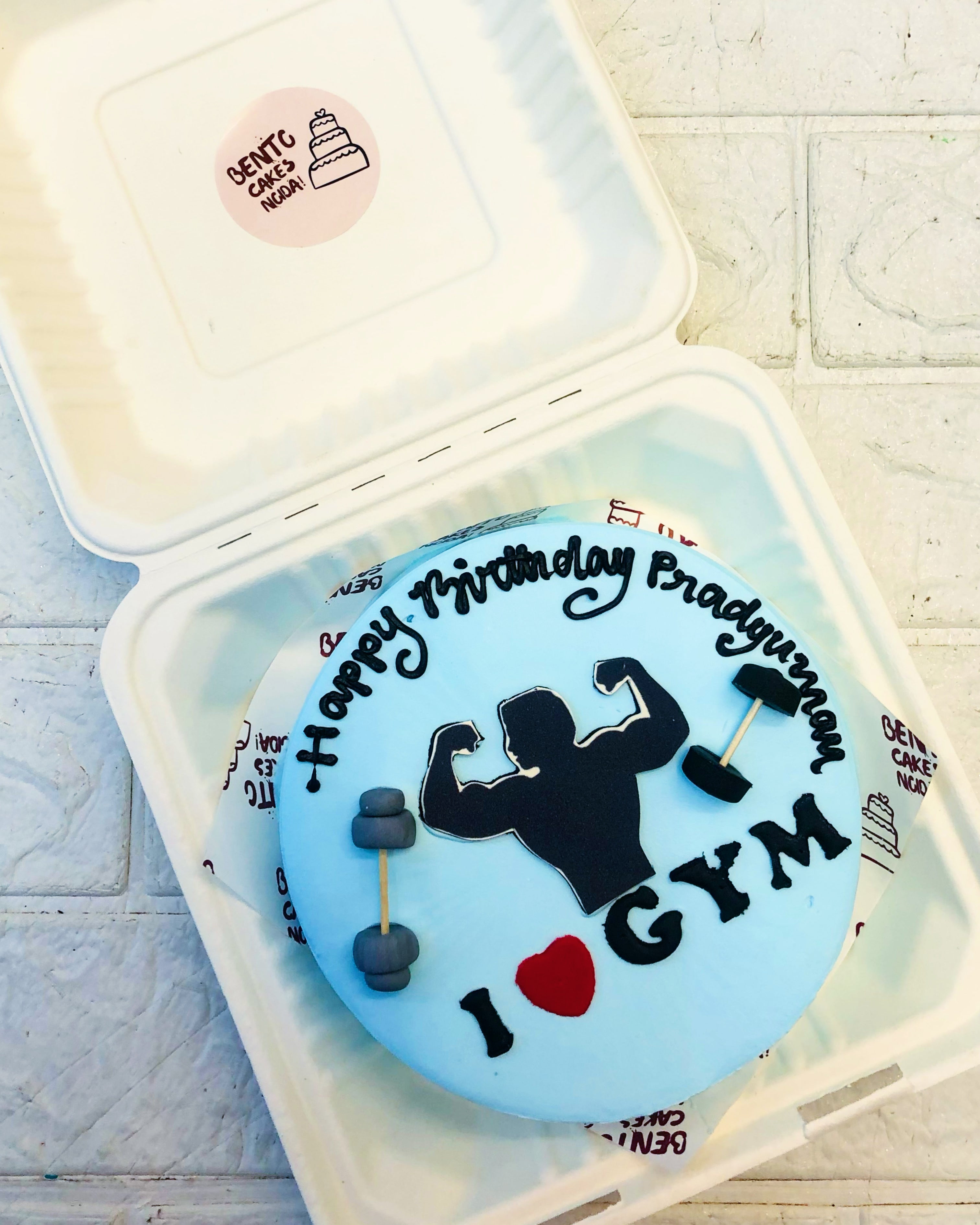 A gym lover blue bento cake showing body with fondant gym dumbles.