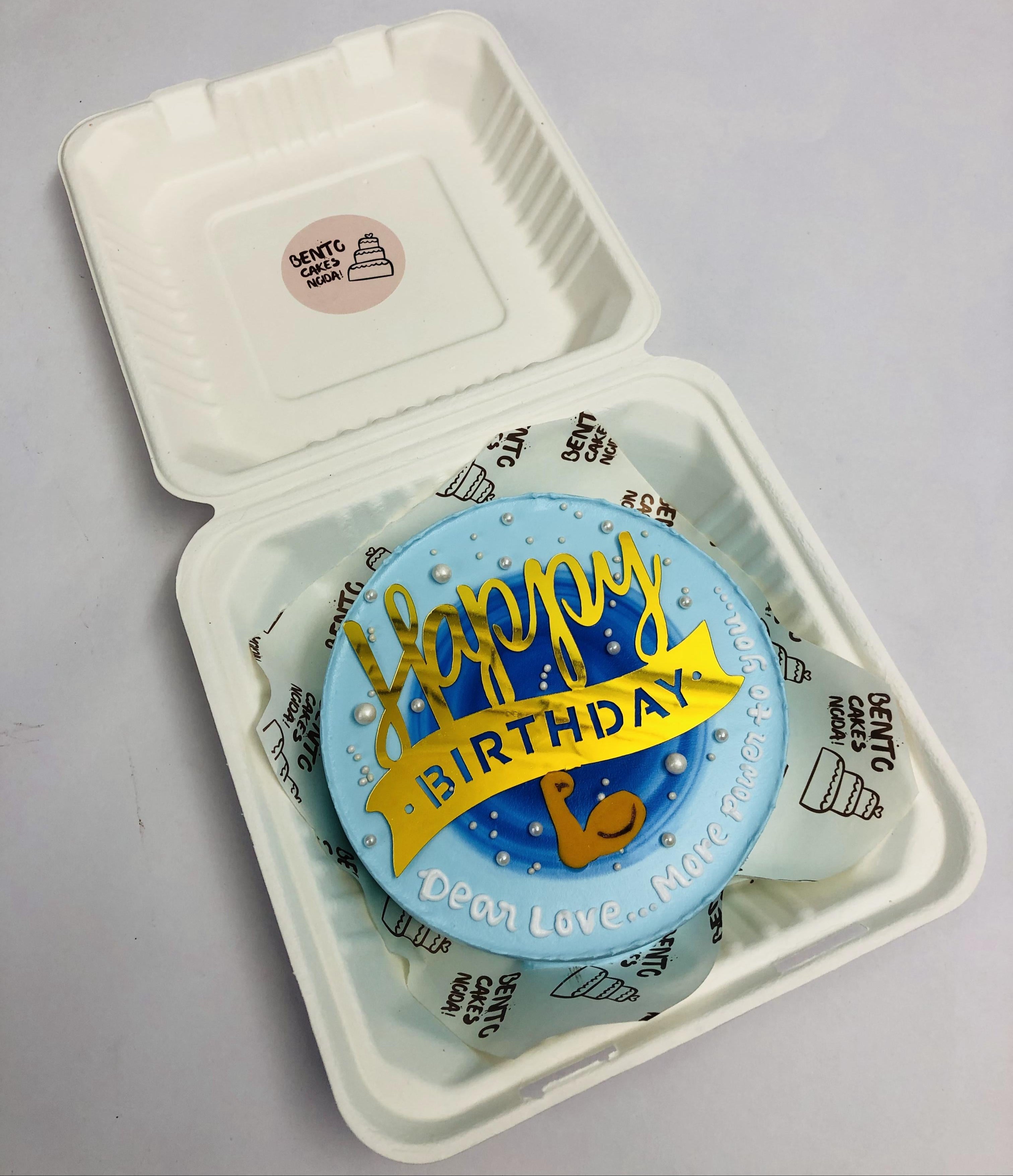 A cool blue bento cake is designed with blue round shade on top with golden happy birthday topper for gym lover's birthday.