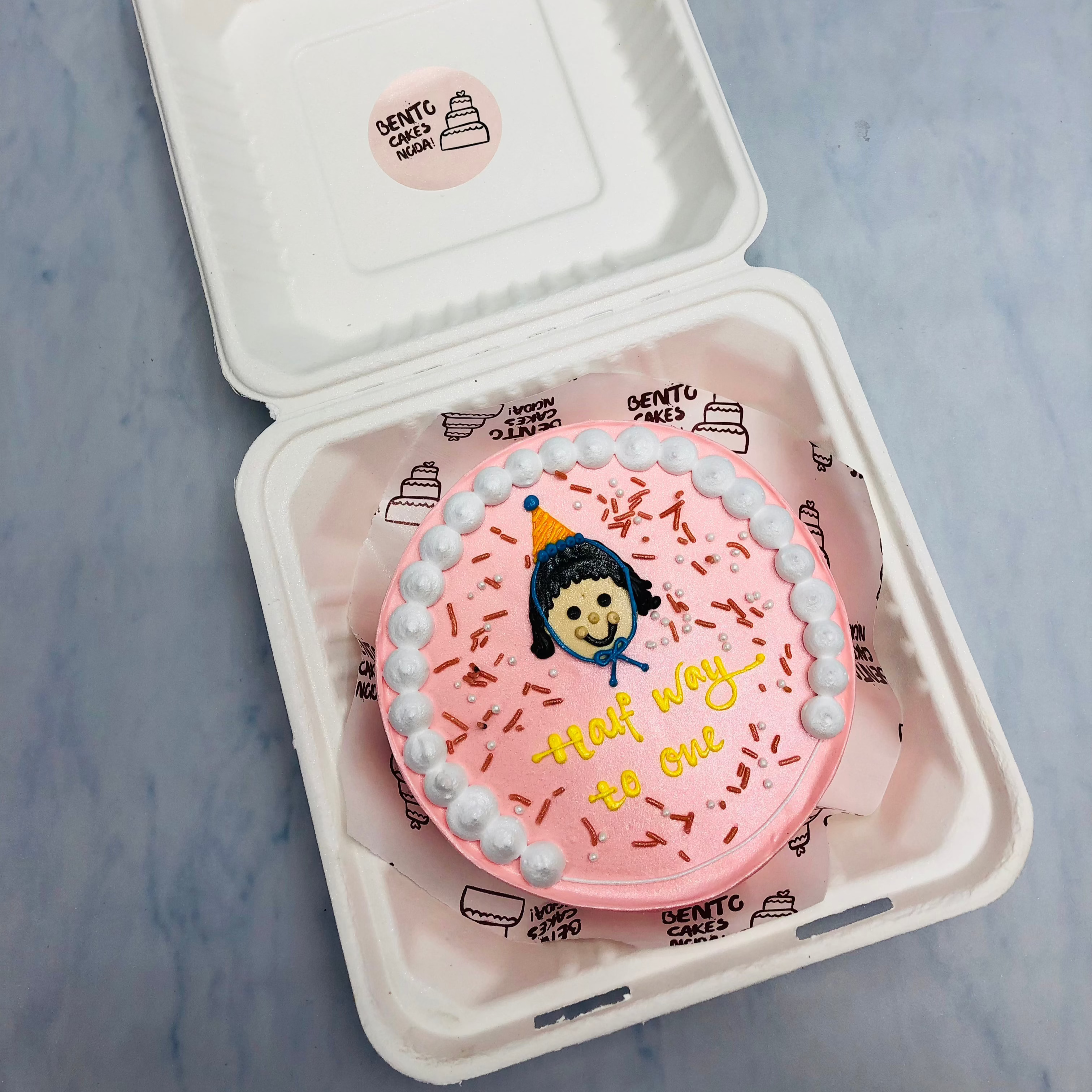 A rose gold cake with a cute cartoon face with white creamy design on its boundary.