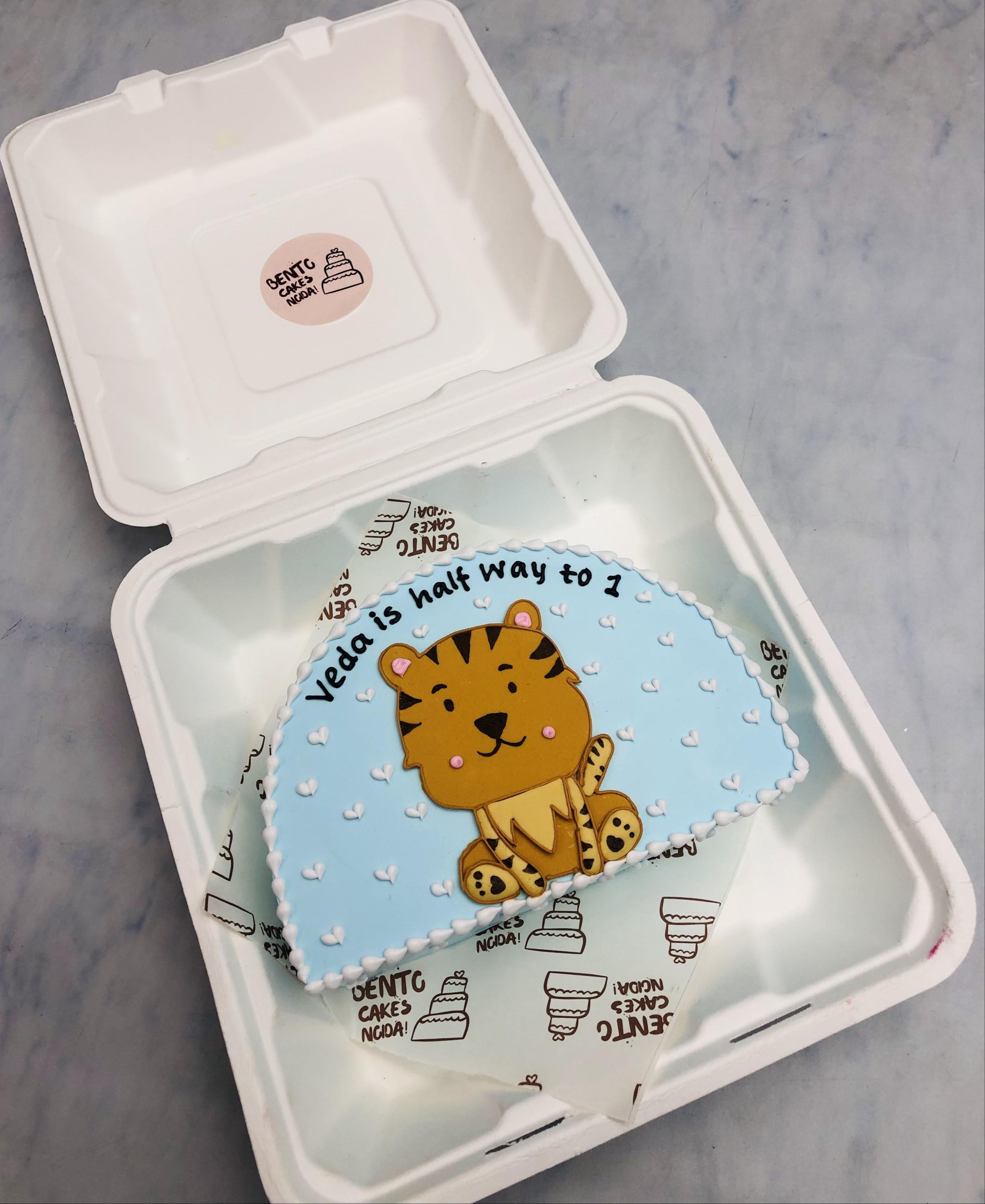 A light blue half shape bento cake having a cute lion design on it.