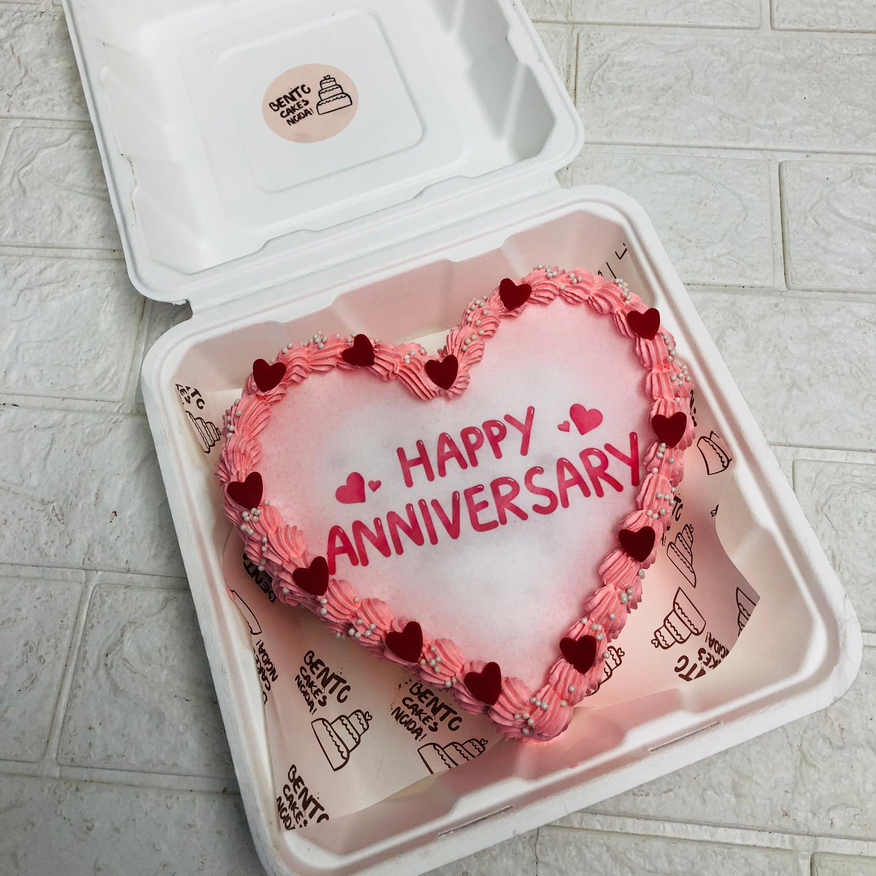 A delightful heart-shaped cake featuring "Happy Anniversary" written on top, ideal for a romantic celebration.