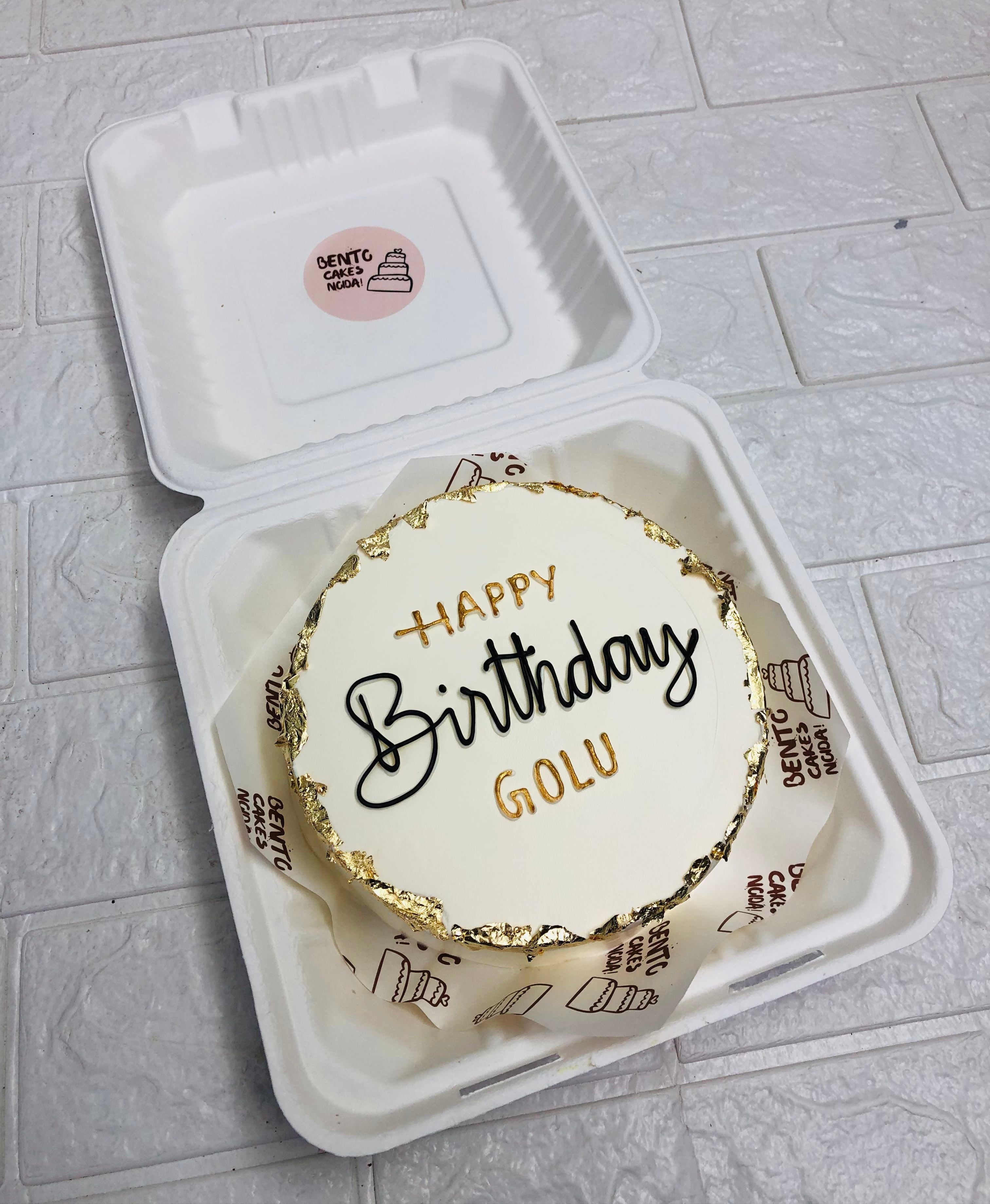 A golden white bento cake is designed for birthday celebration with golden work on its boundary.