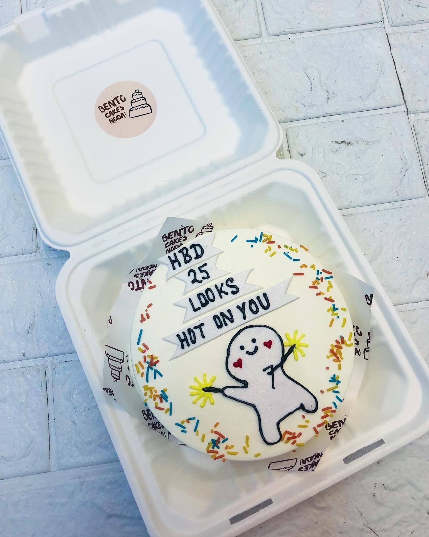 A white bento cake having a cute cartoon design holging crackers and a text written on fondant.