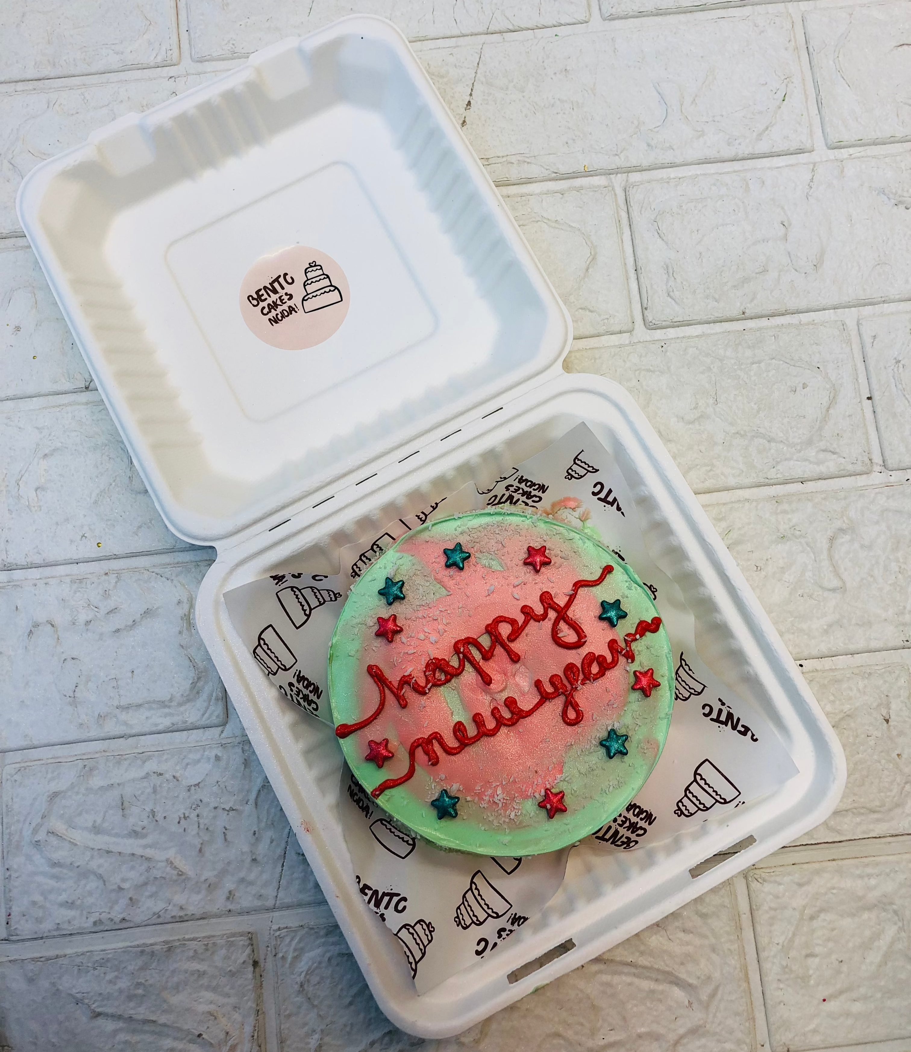 A lime green bento cake having red shapes design on top and decorated with red and blue stars.