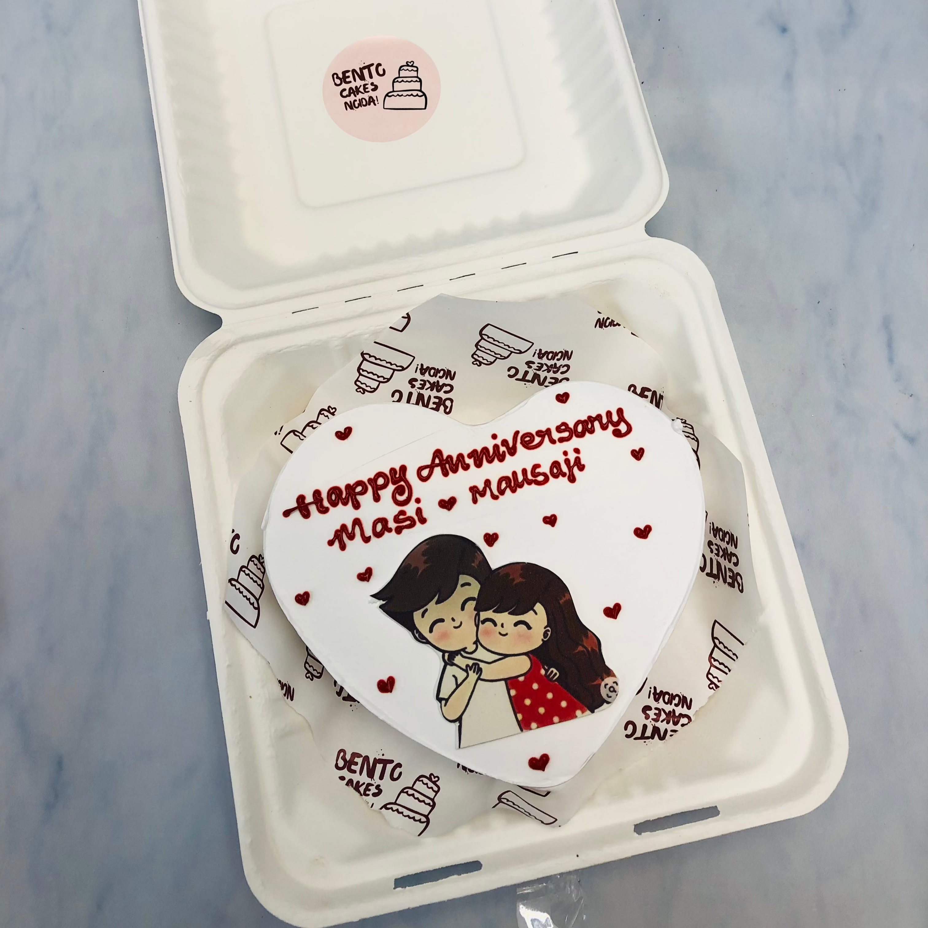 A white heart shape cake with loving couple print and filled with red hearts desgns.