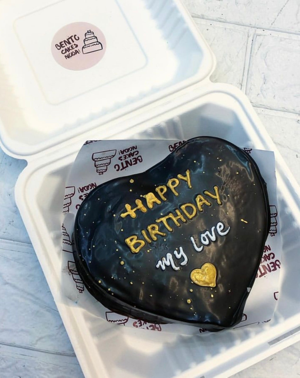 A chocolatey heart shape cake with golden and white tet on cake.
