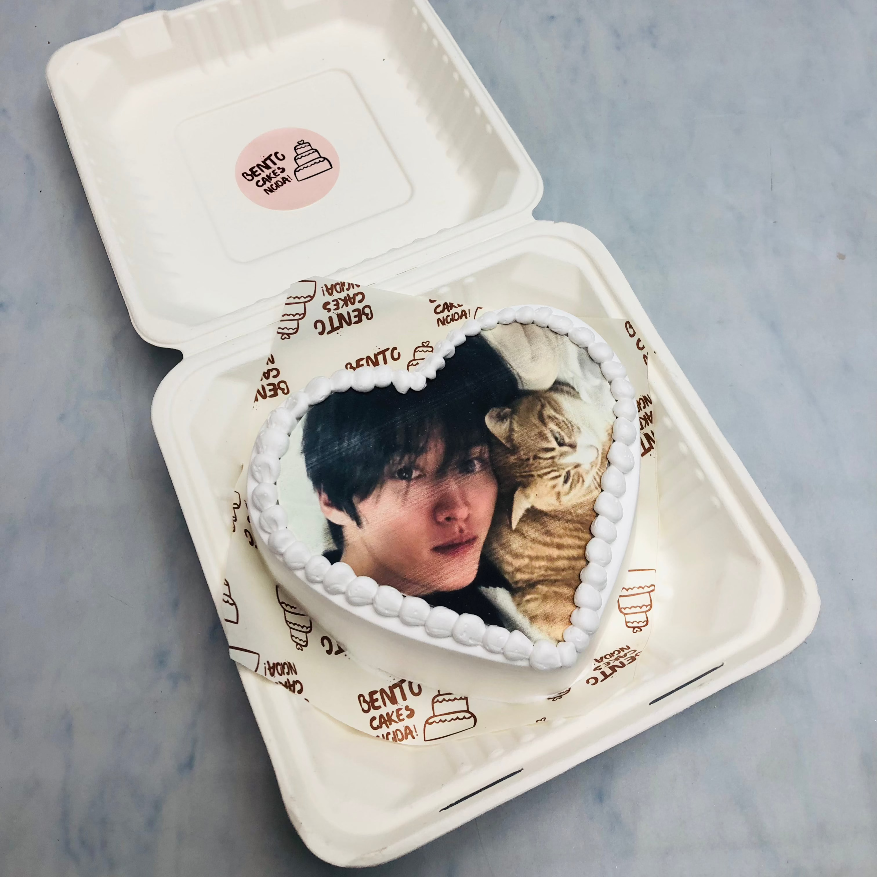 A white heart shape bento cake with a boy and a cat photo on it.
