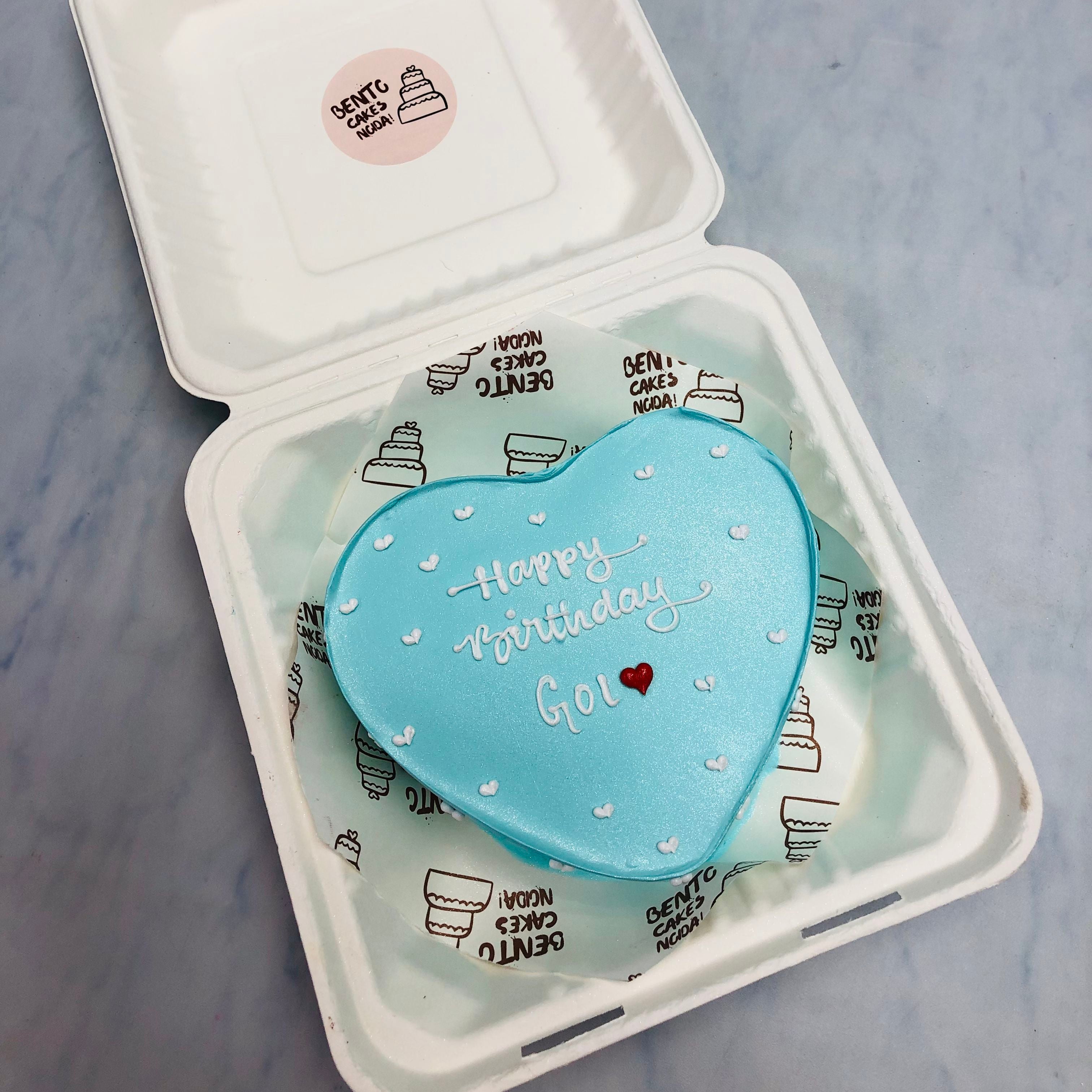 A sky blue heart shape cake with "Happy Birthday" text written on it with white icing.