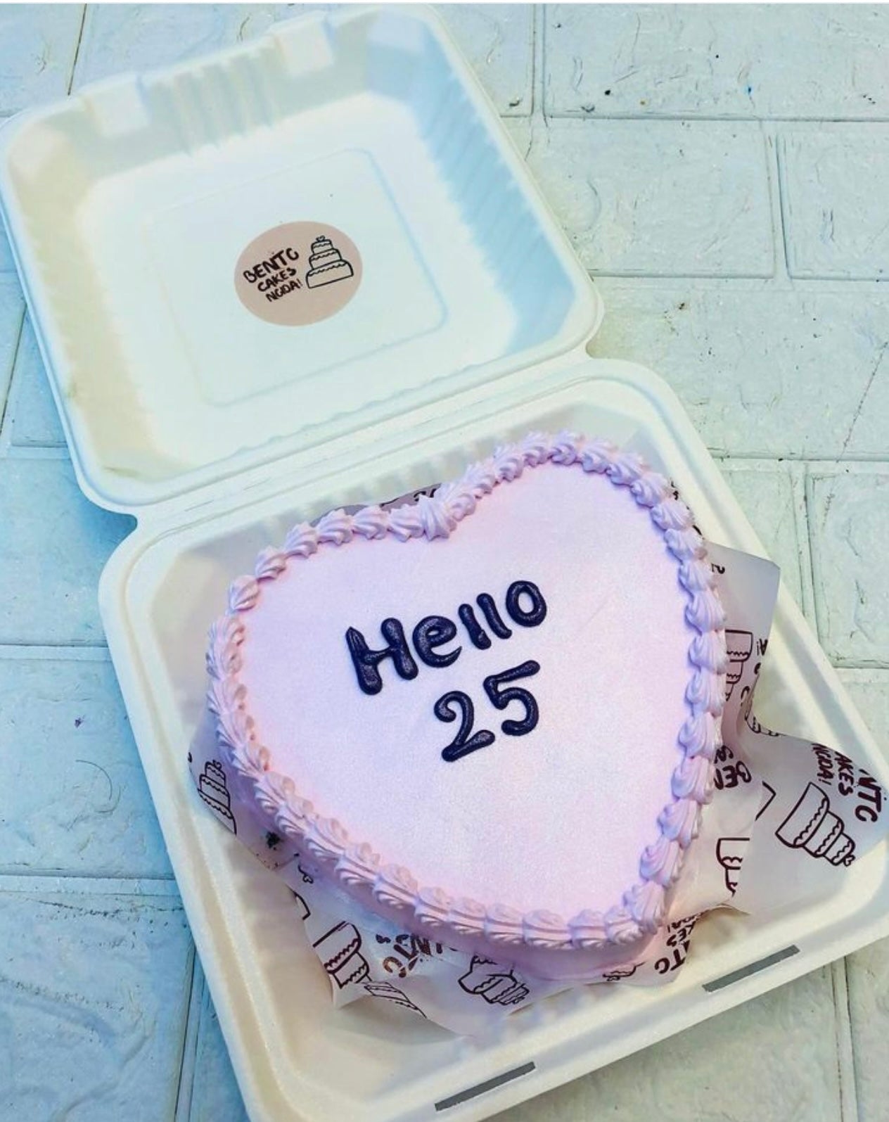 A light pink hert shape cake with "Hello 25" text on it.