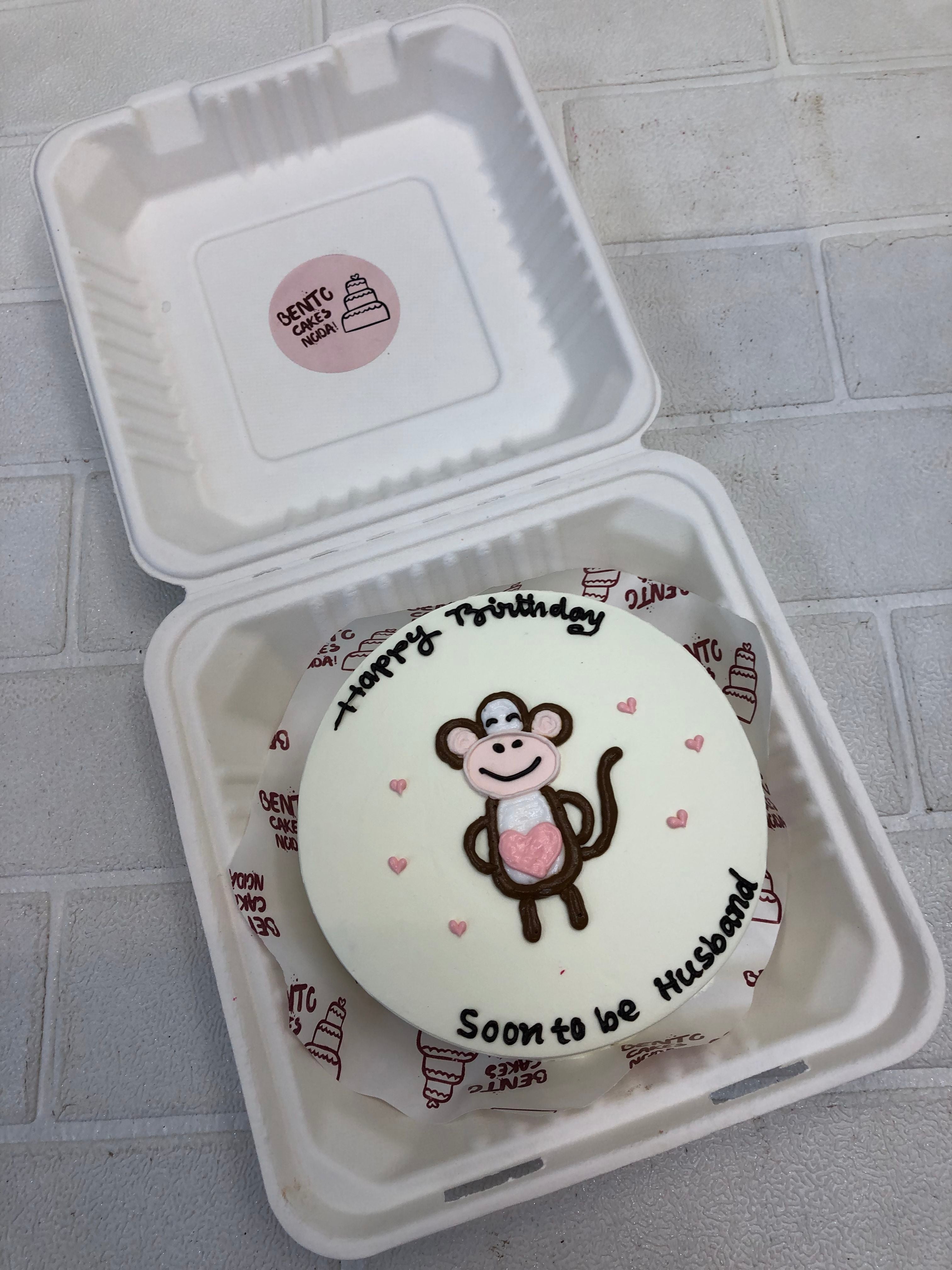 A white bento cake having a cute monkey drawing with light pink hearts on it's side and a cute text "Husband to be" written with black color.