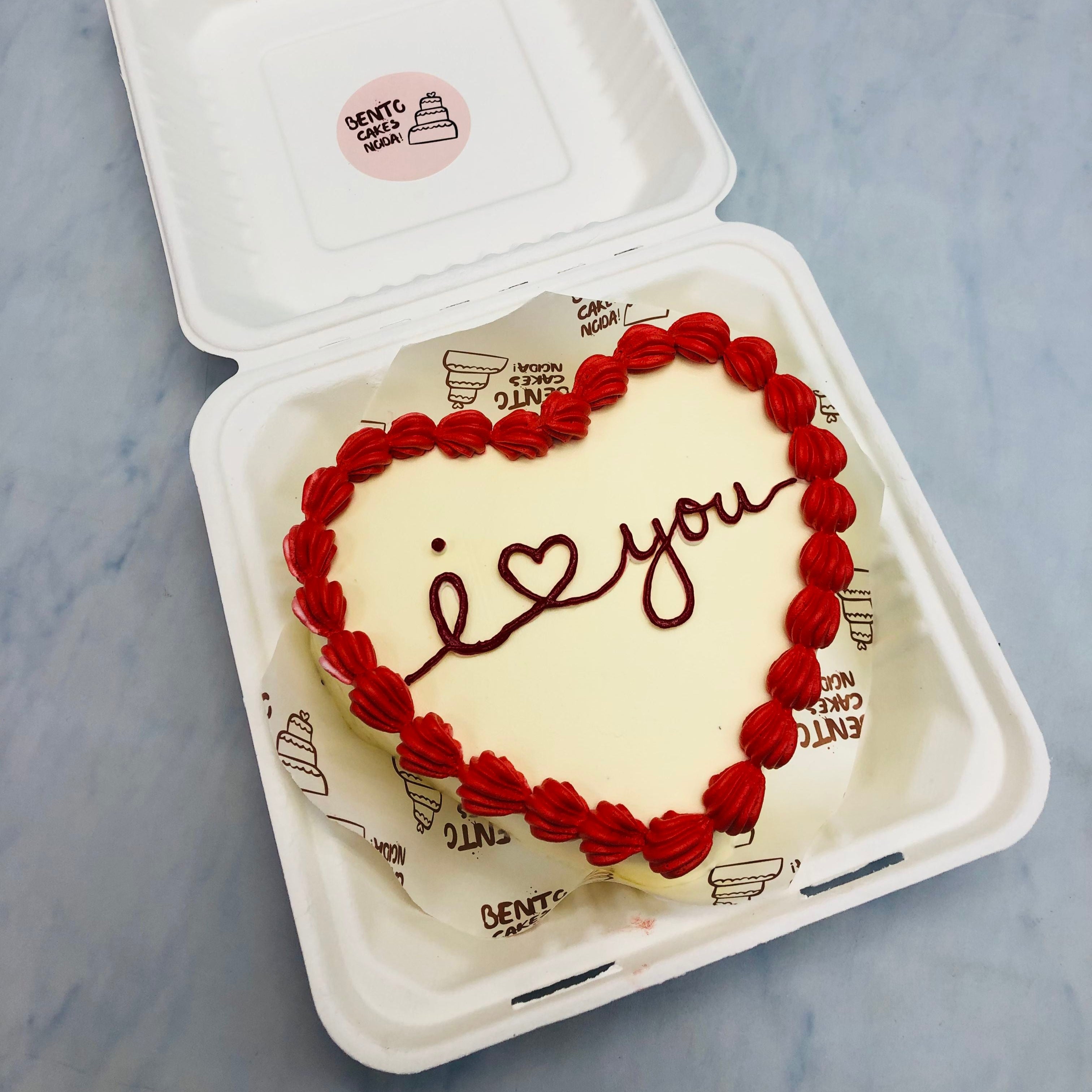 AN offwhite heart shape cake with red boundries and a "I Love Yoy" text written in the center of cake.
