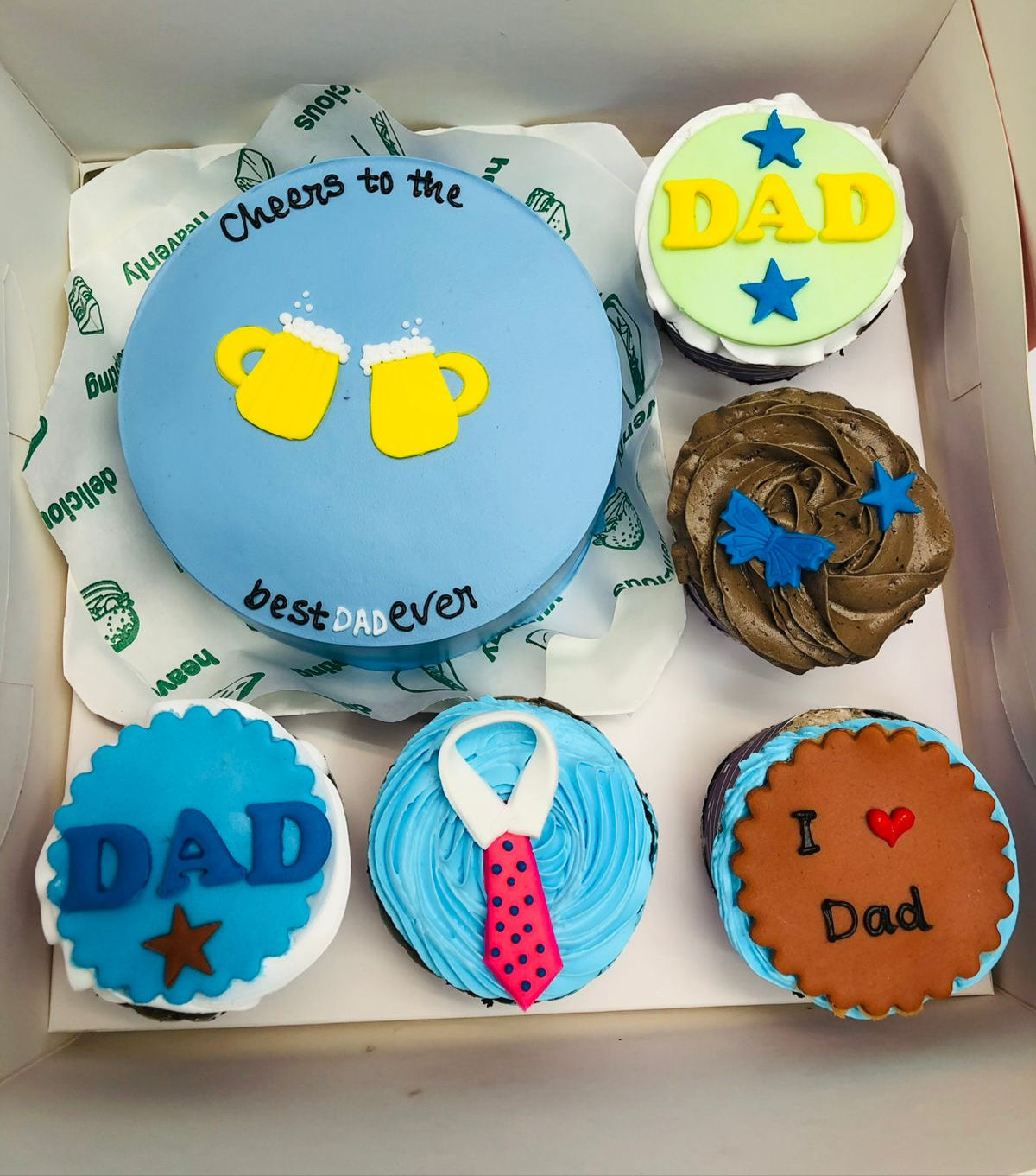 A light blue cake with cheers design and  5 cupcakes with different design.