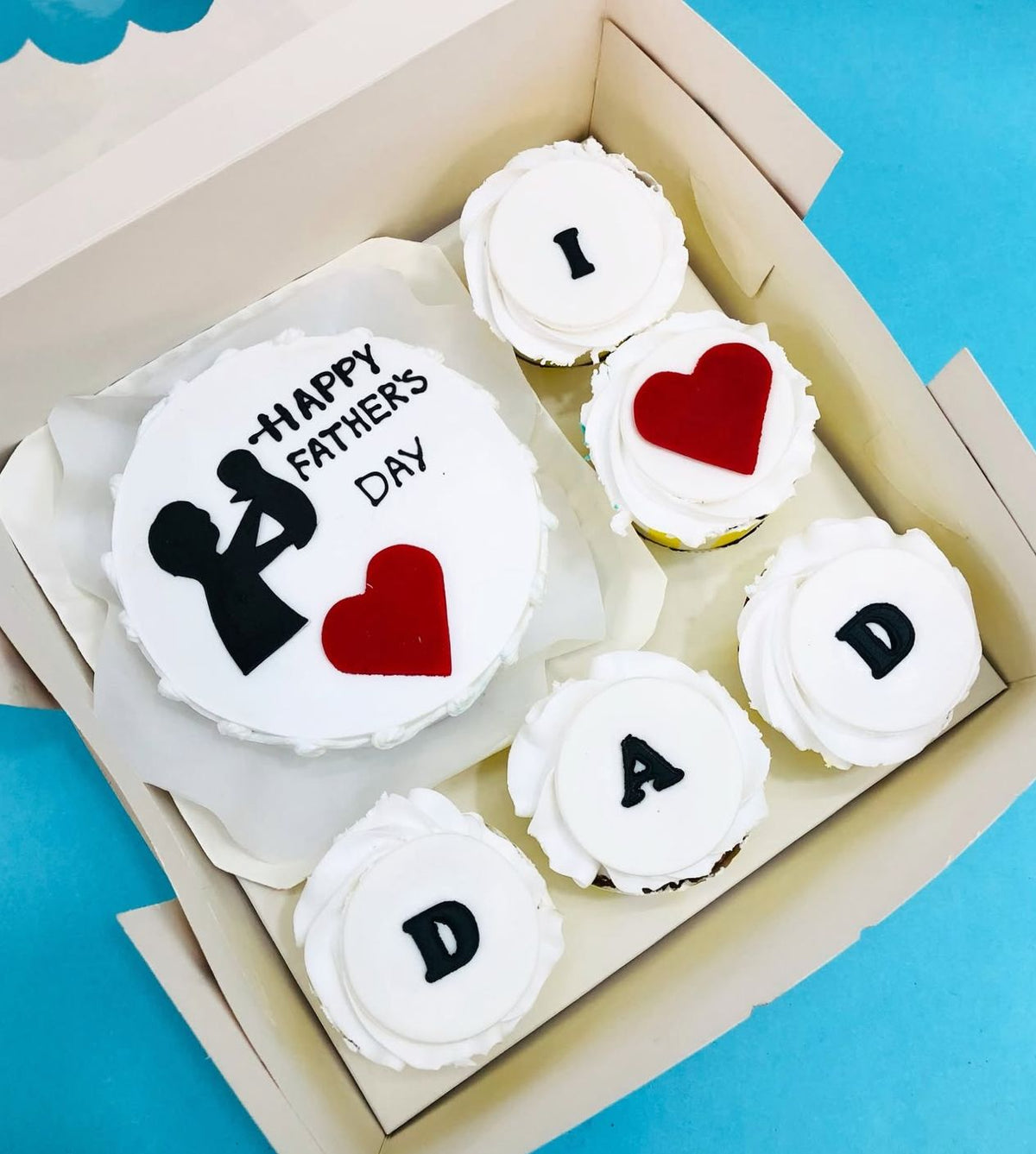A white bento cake with father and baby design and 5 cupcakes with different designs.