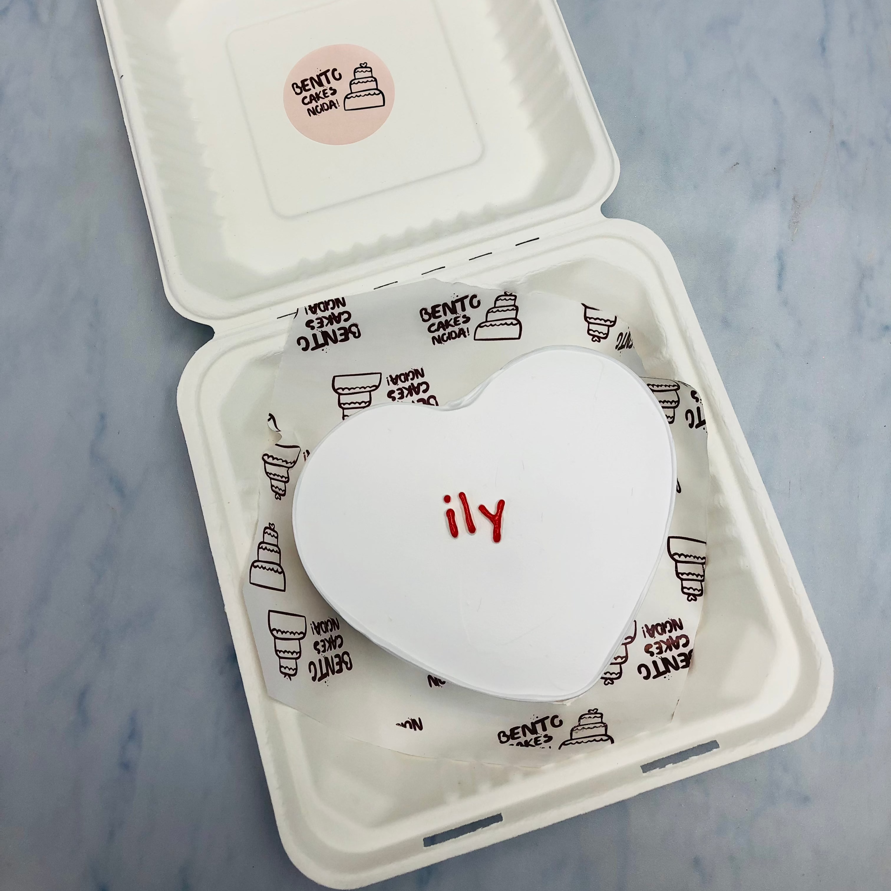 A pure white heart shape cake with a cute text "ily" written with red color in the centerb of the cake.