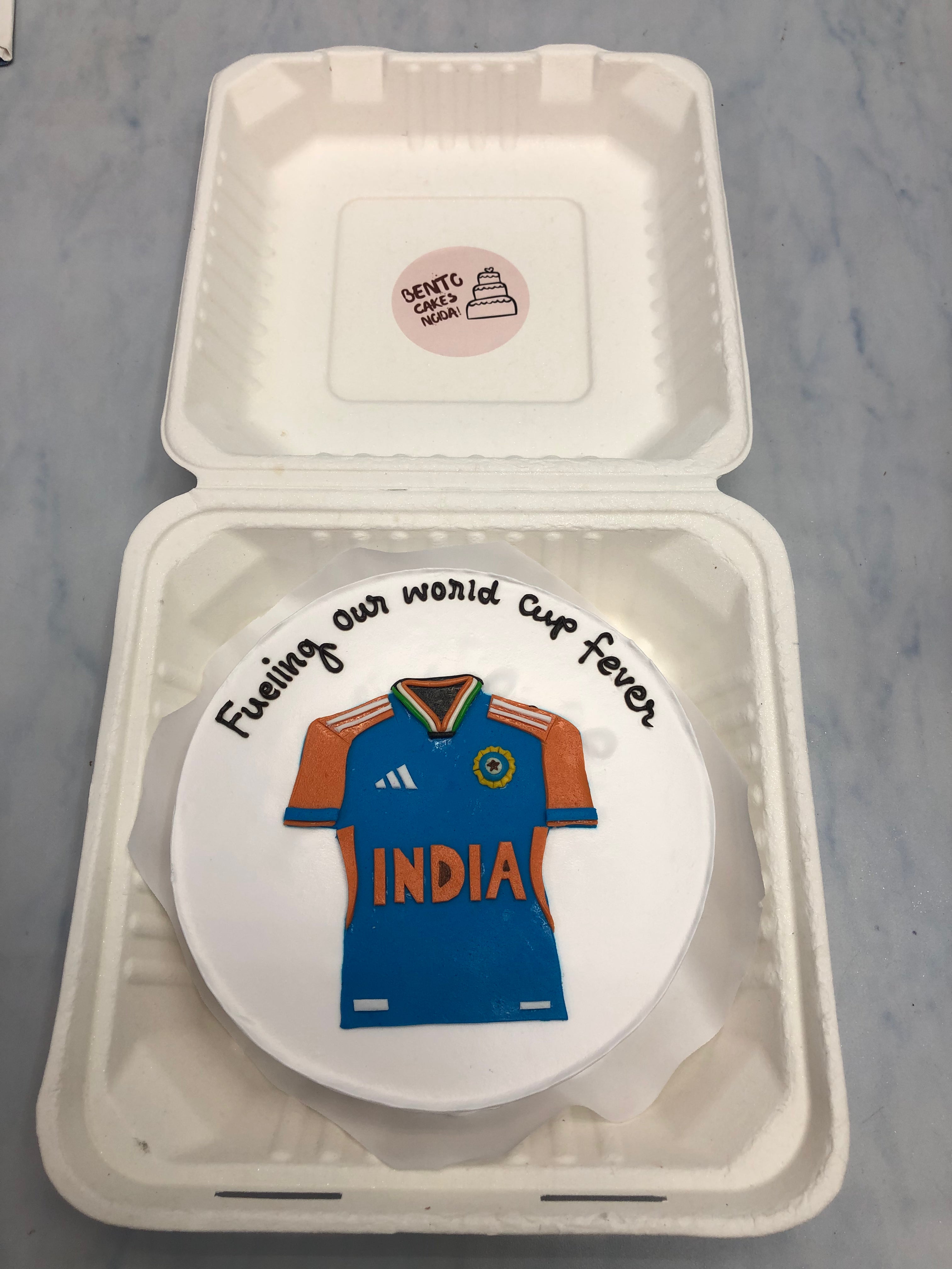 A white bento cake having indian cricket theme jersey.