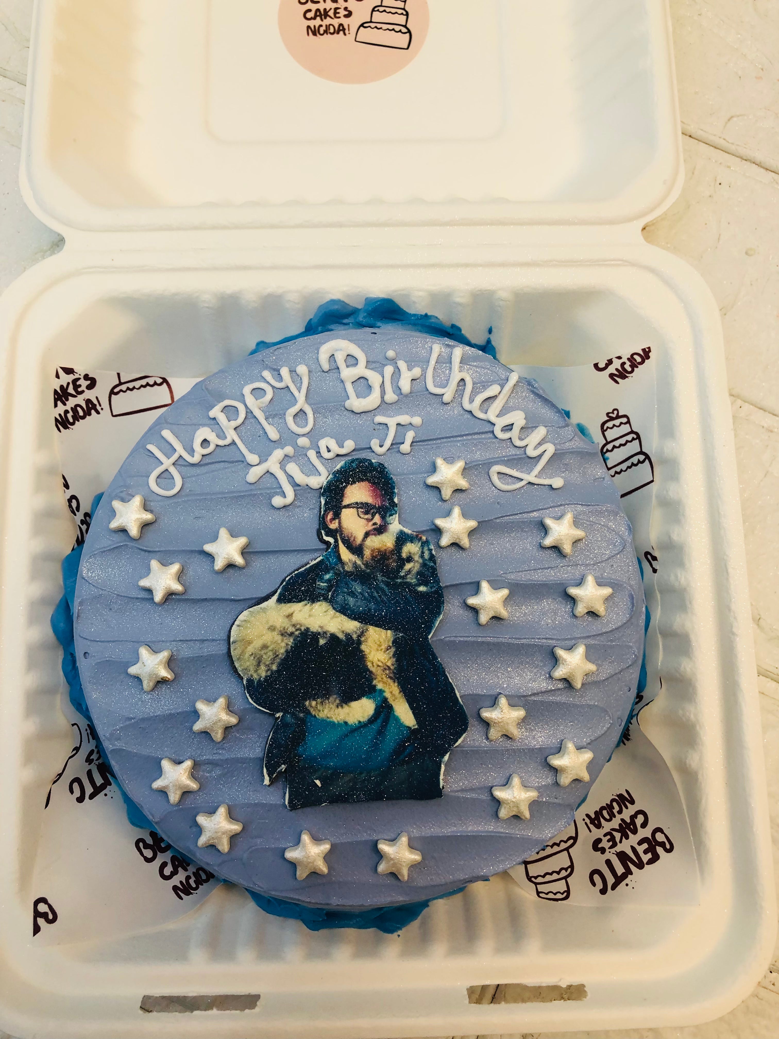 A shiny blue bento cake with white fondant stars and a print of a man with his dog.