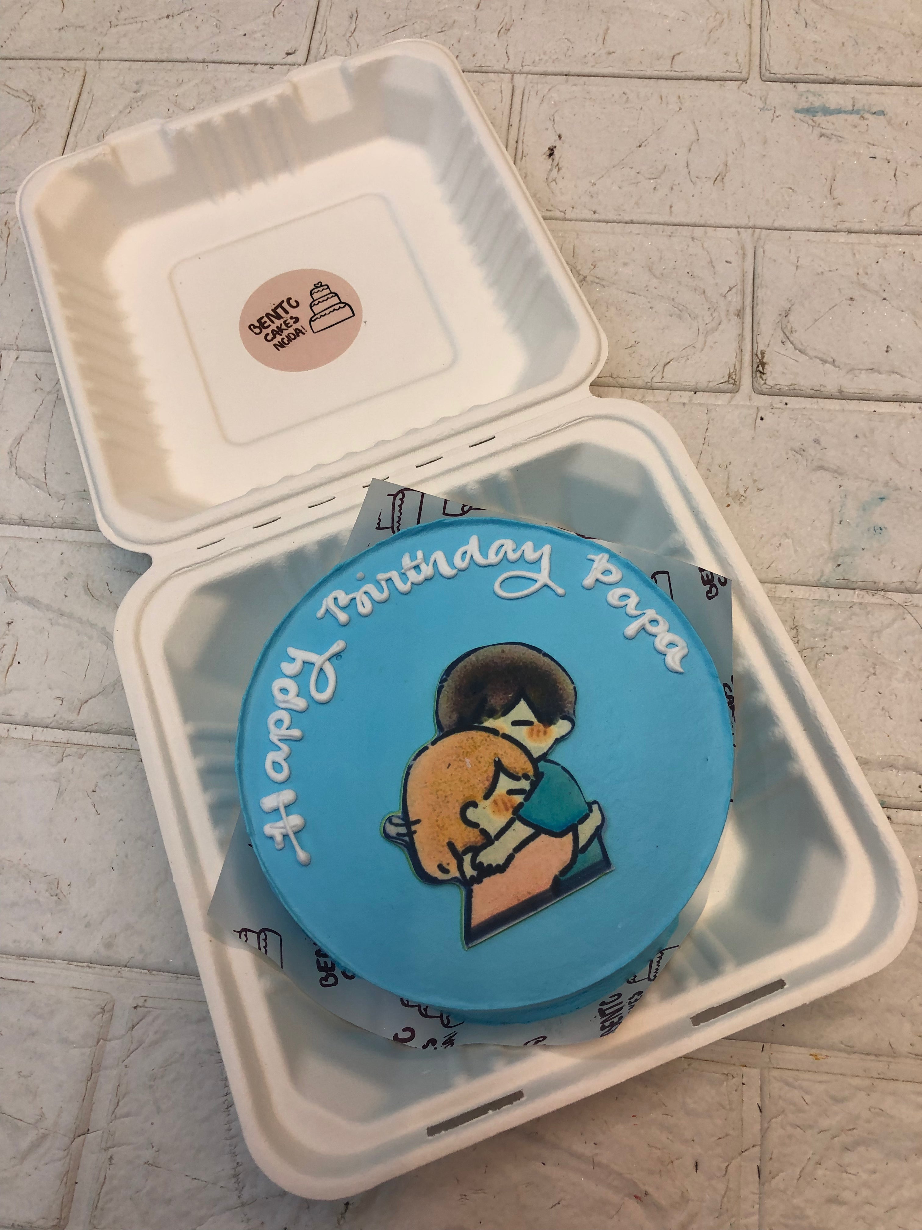 A blue icng on bento cake with a hugging couple drawing of a father and baby.