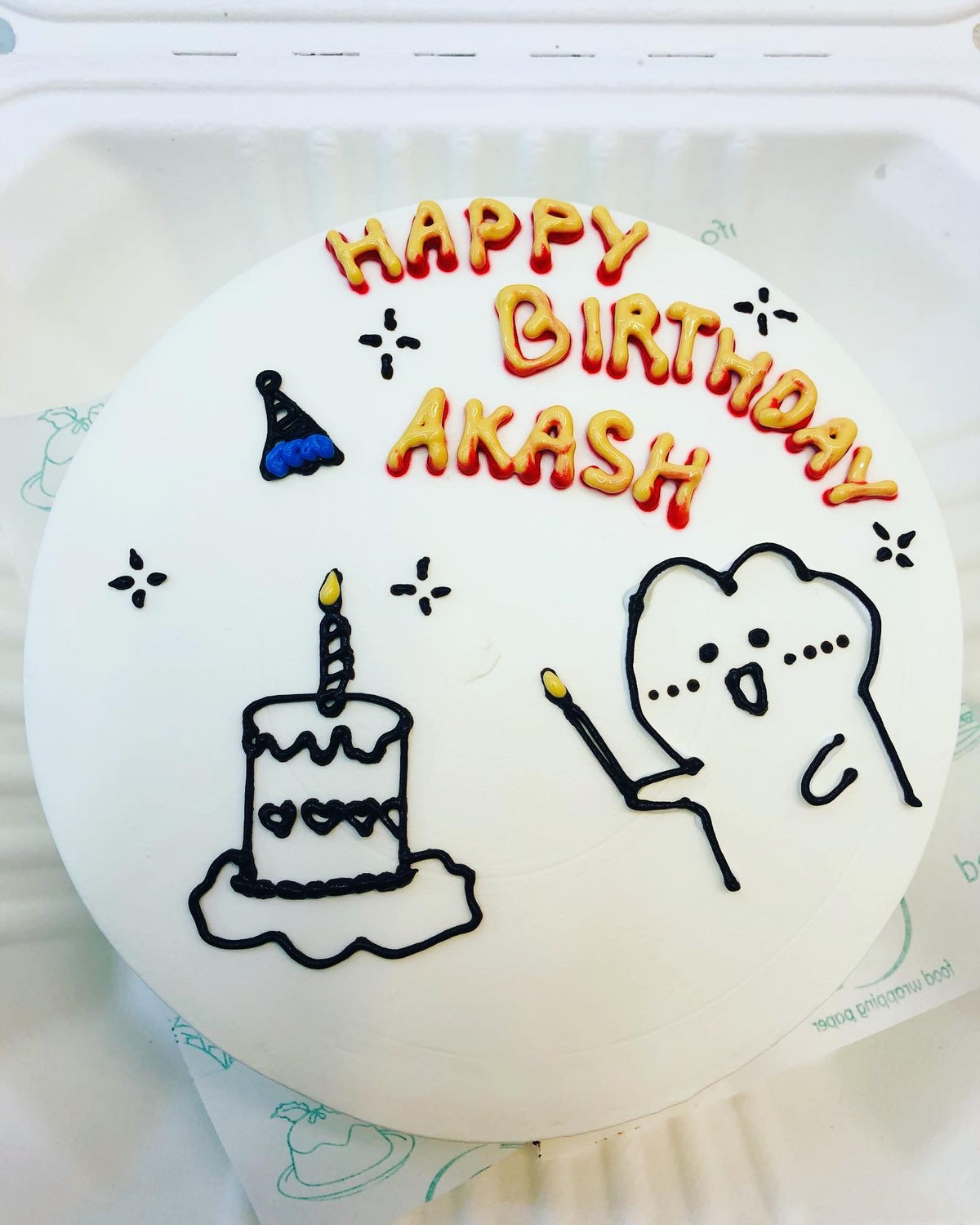 A white cake with a cartoon celebrating birthday and glowing a candle on cake, a text "HAPPY BIRTHDAY AKASH" beautifully written on it.
