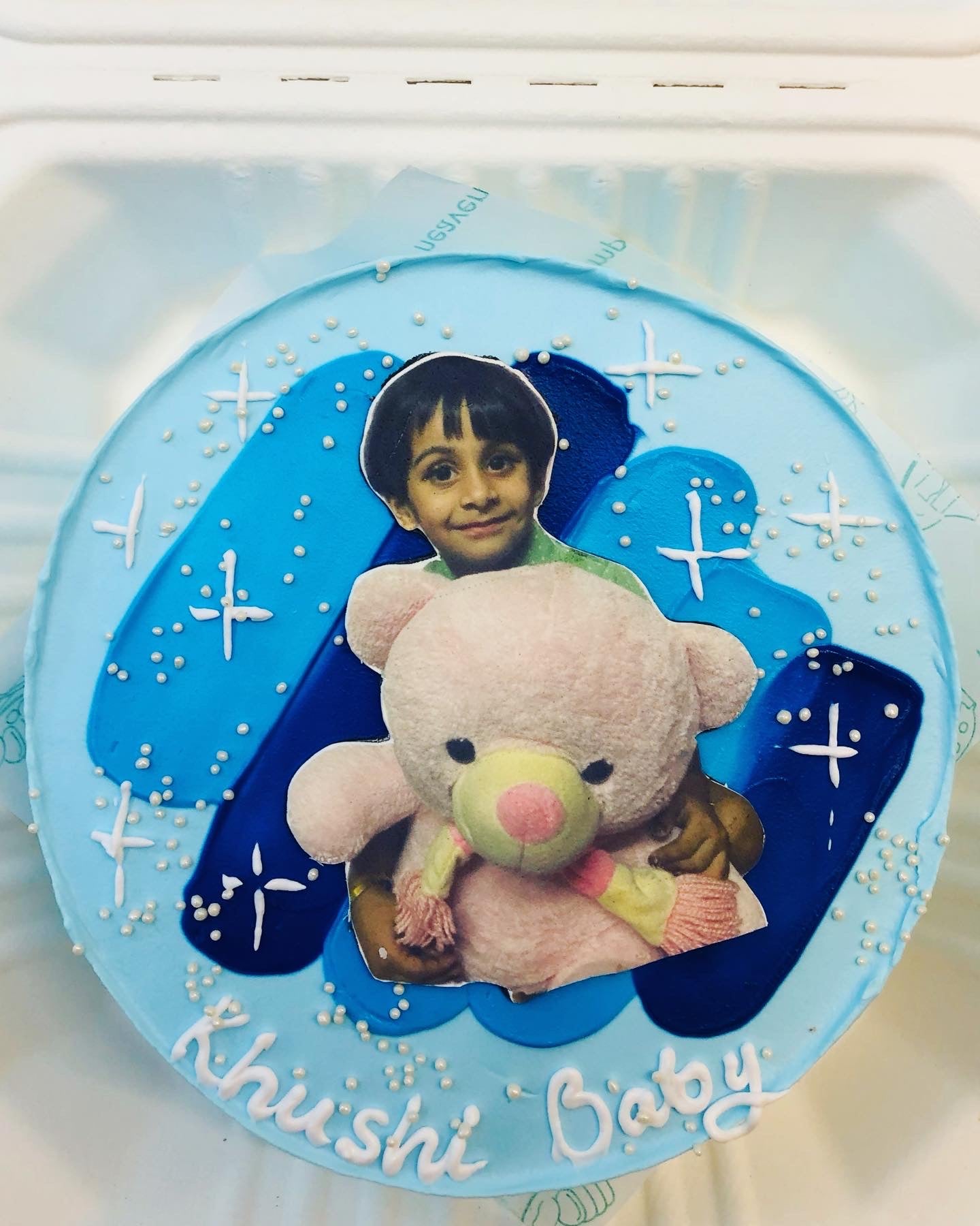 A sky-blue cake decorated with dark blue icing on it and a picture of kid with teddy placed on it.  